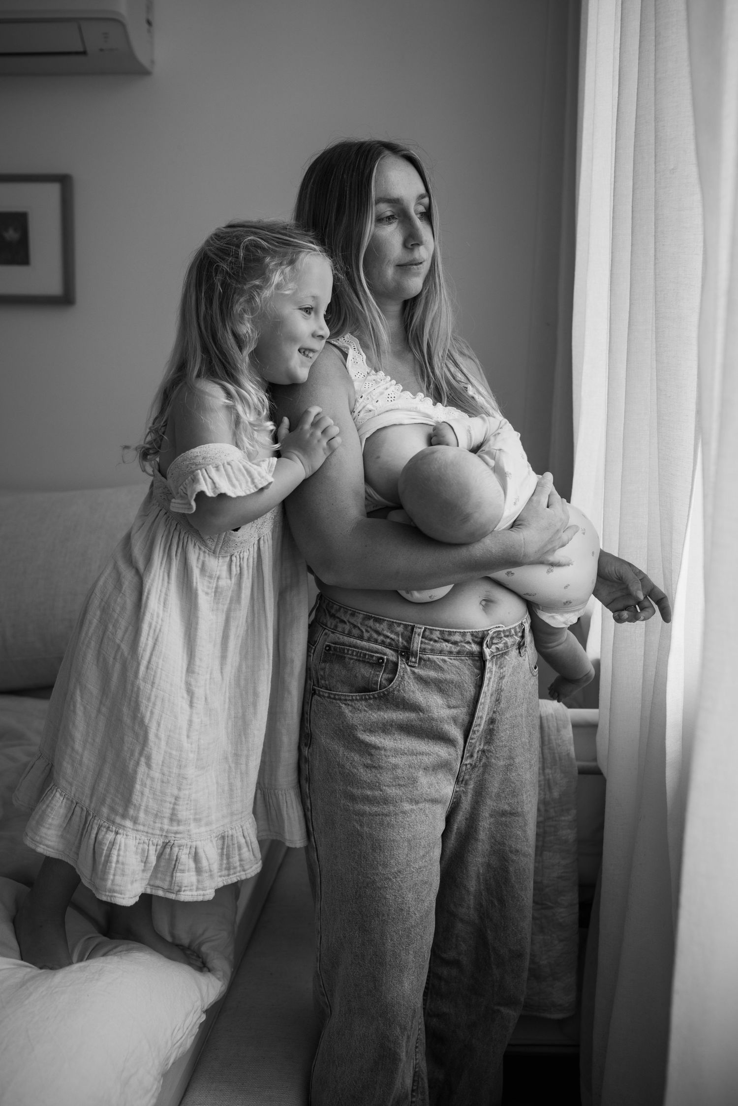 Black and white series of tender family moments by a window.