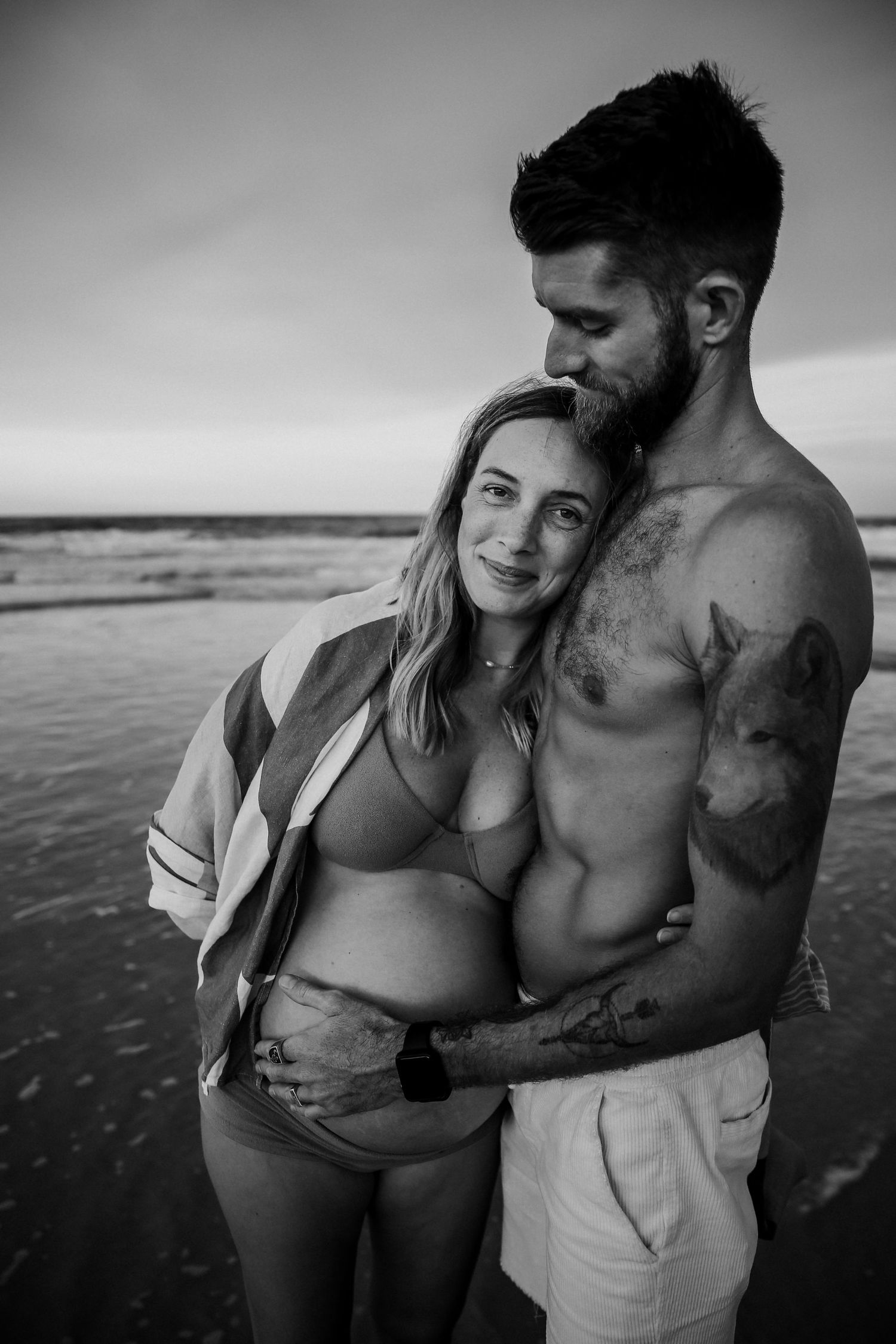 Black and white romantic beach photos of a couple embracing in swimwear at sunset.