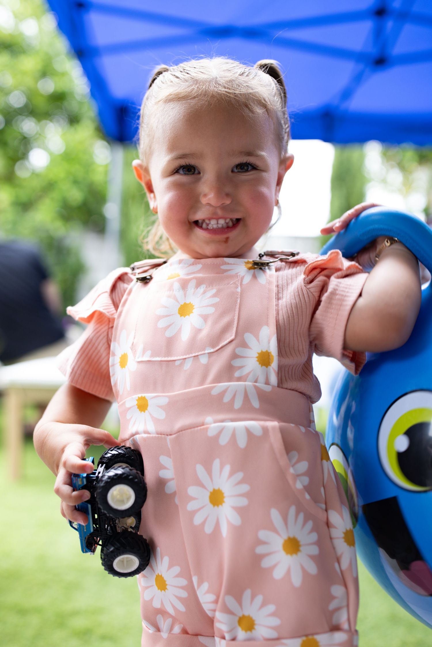 Baby wearing pink floral outfit smiling and playing with toys outdoors.
