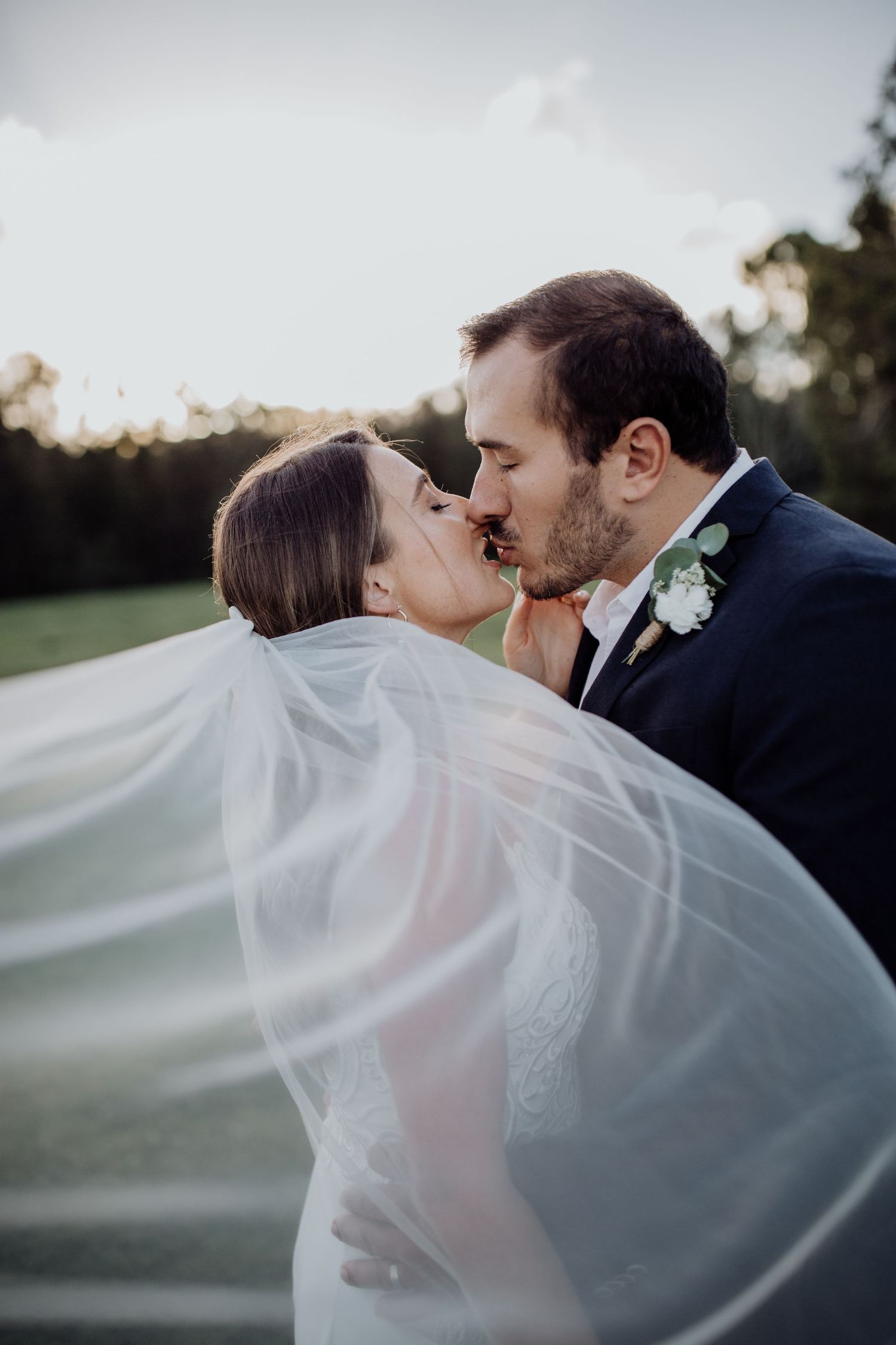 Romantic wedding portraits with flowing veil captured during golden hour.