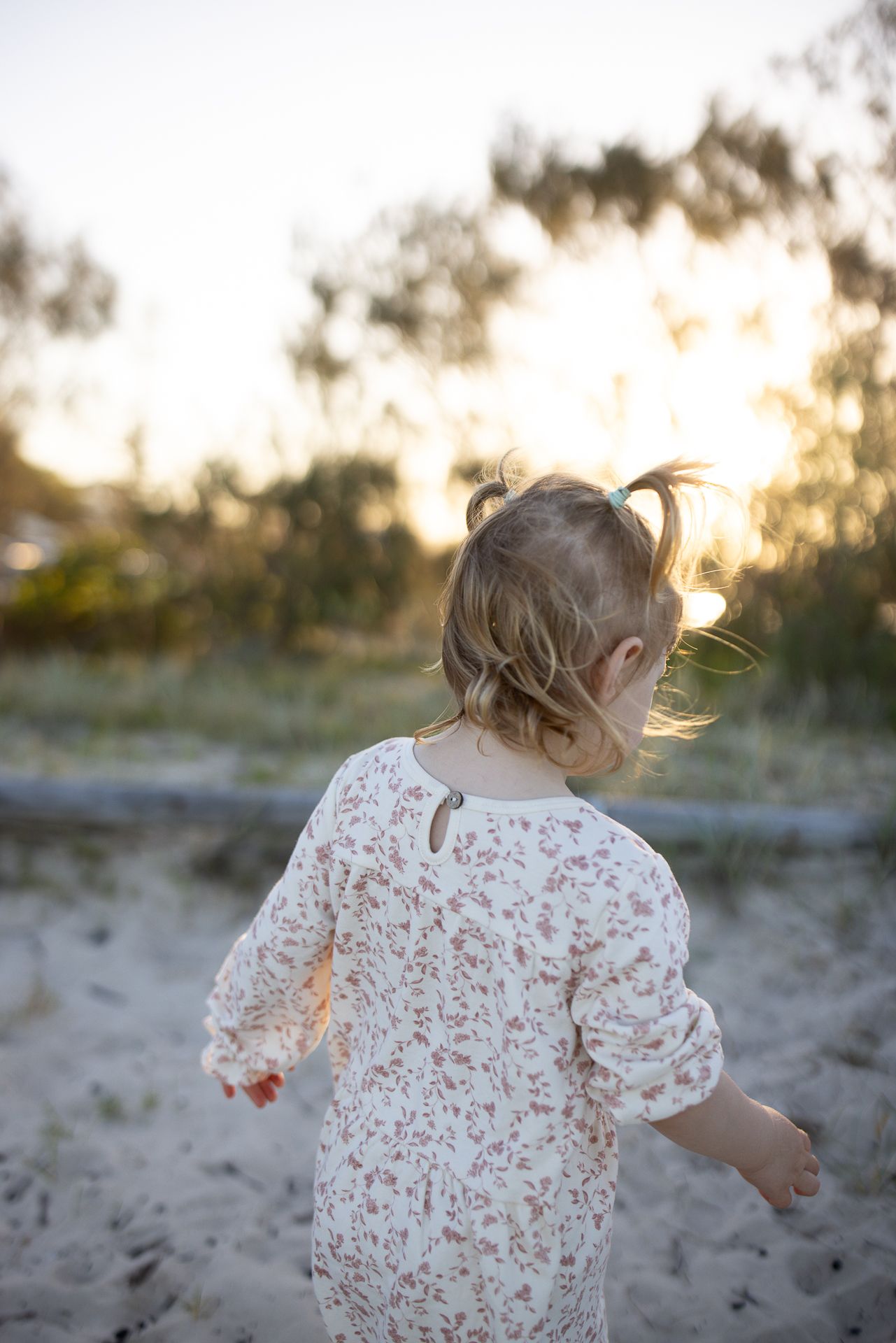 Child in a floral dress running and playing on the beach at golden hour.