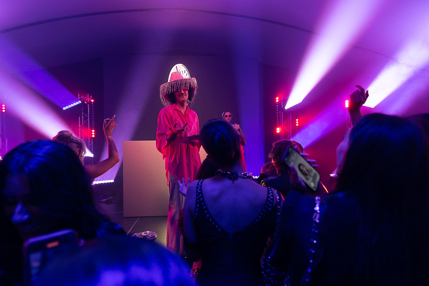 Concert stage illuminated with vibrant purple and pink lighting effects creating an atmospheric performance environment.