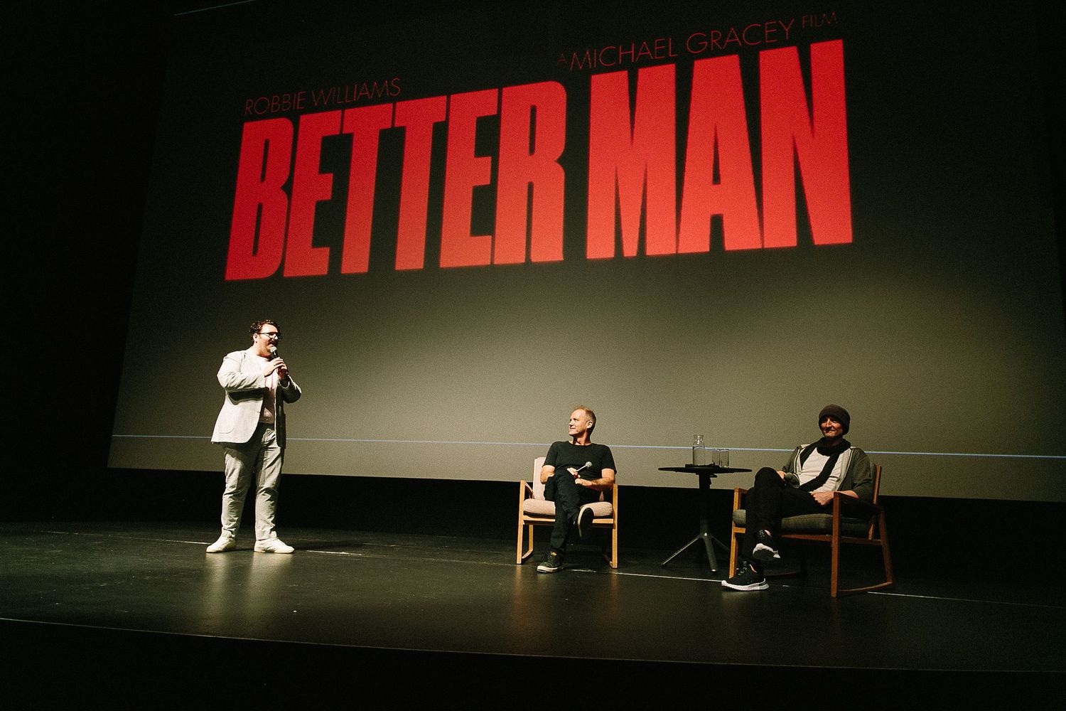 Theater stage setup with red text 'BETTER MAN' displayed prominently against dark background.