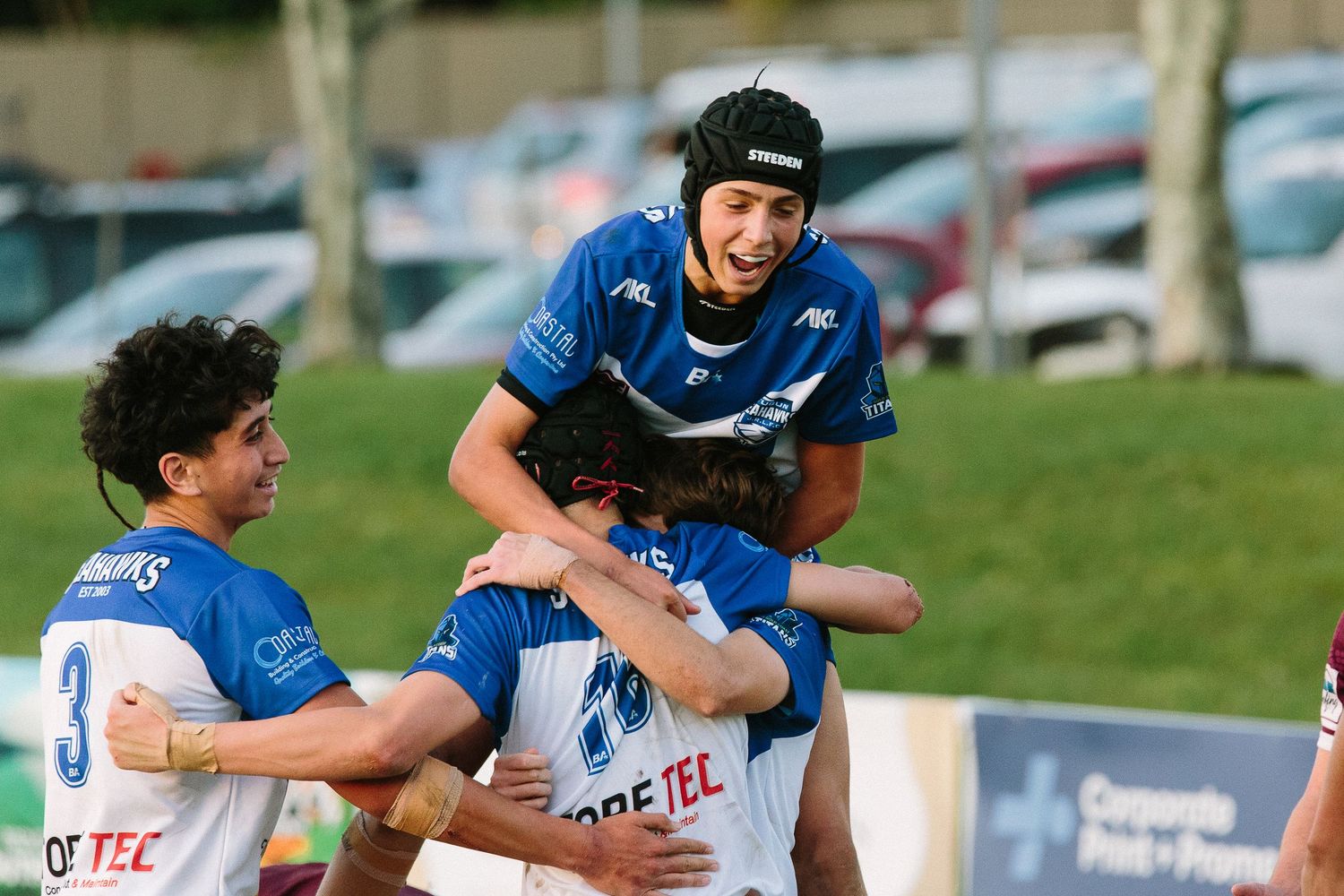 Sports team players in blue jerseys celebrating together on a sunny field.