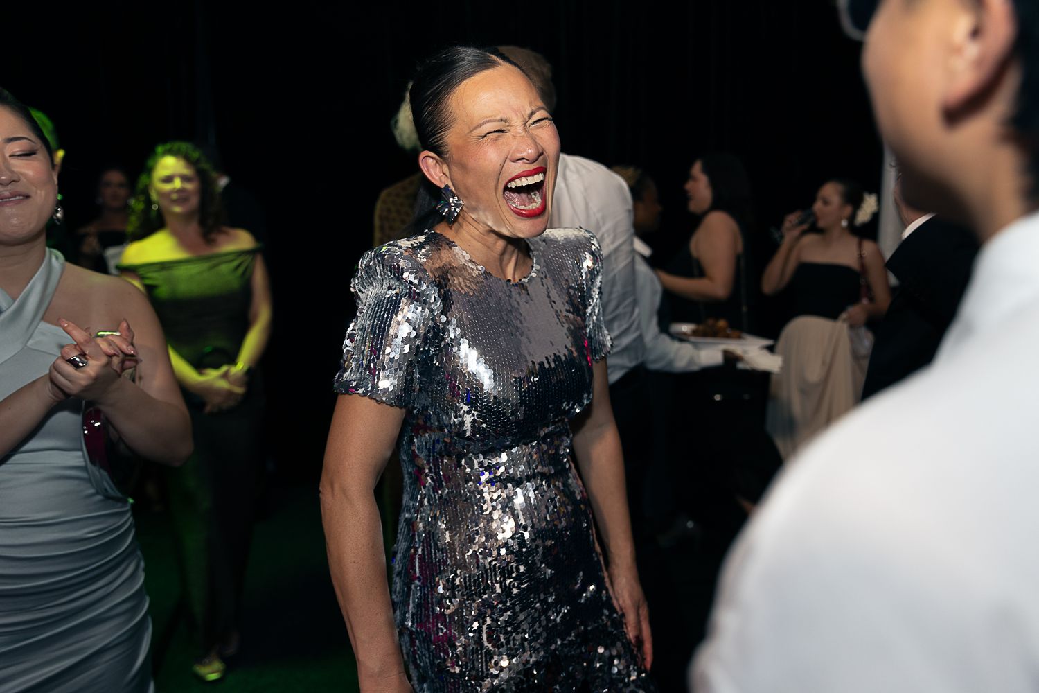 Party guests dancing and laughing together at a lively nightclub event with colorful lighting.