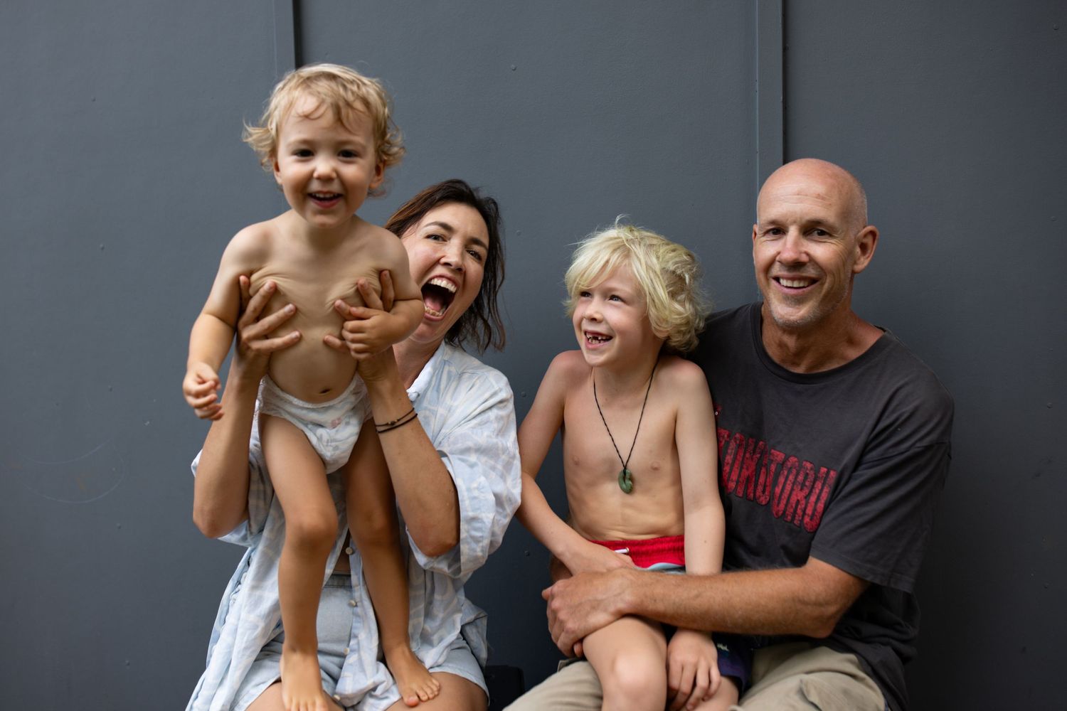 Family playing and laughing together against a dark grey wall.