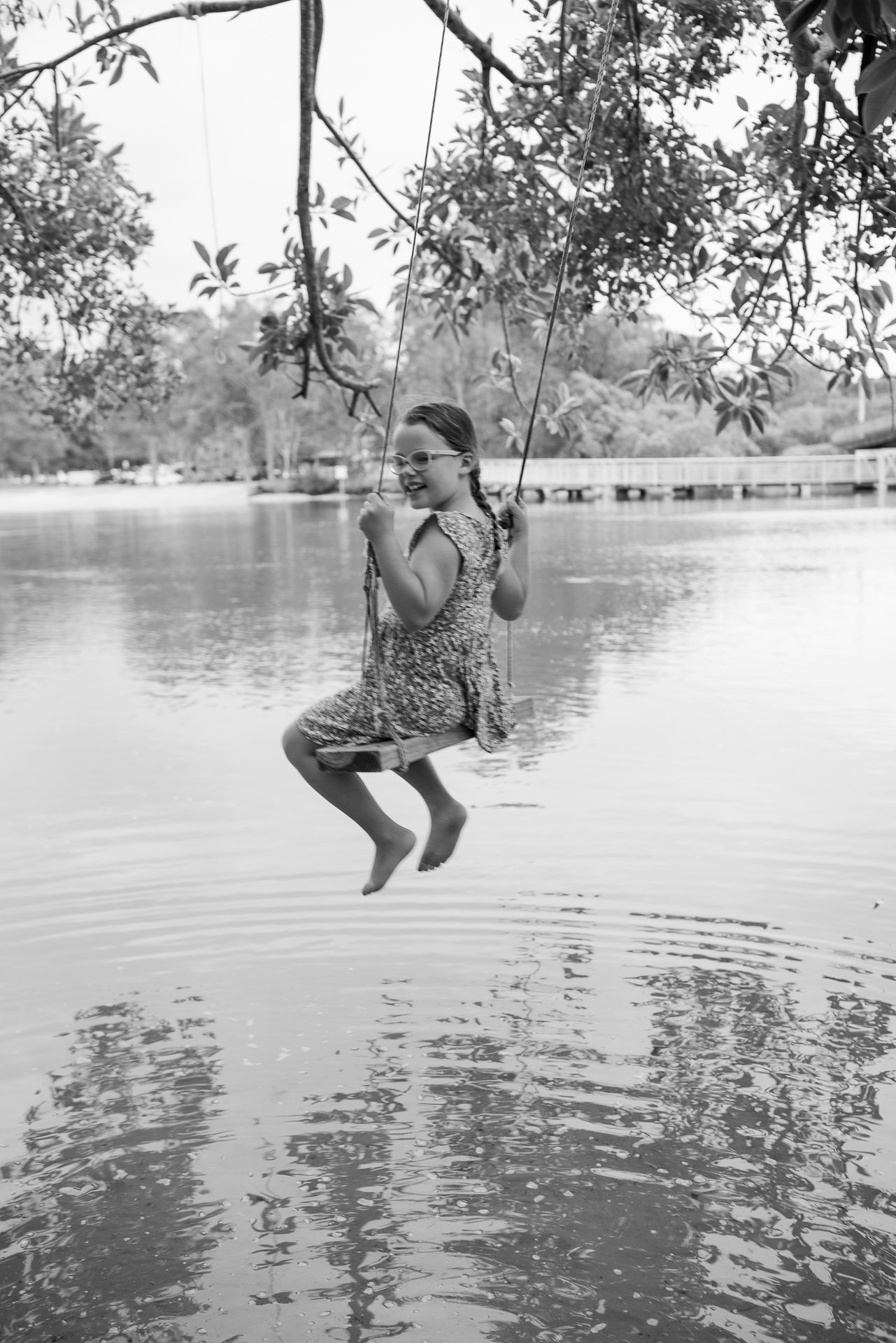 A black and white photo of someone swinging on a rope over water.