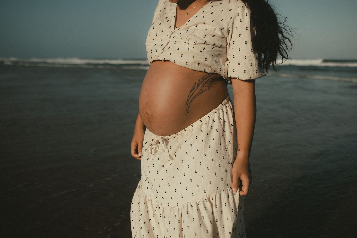 Maternity photos on the beach featuring a flowy polka dot dress.