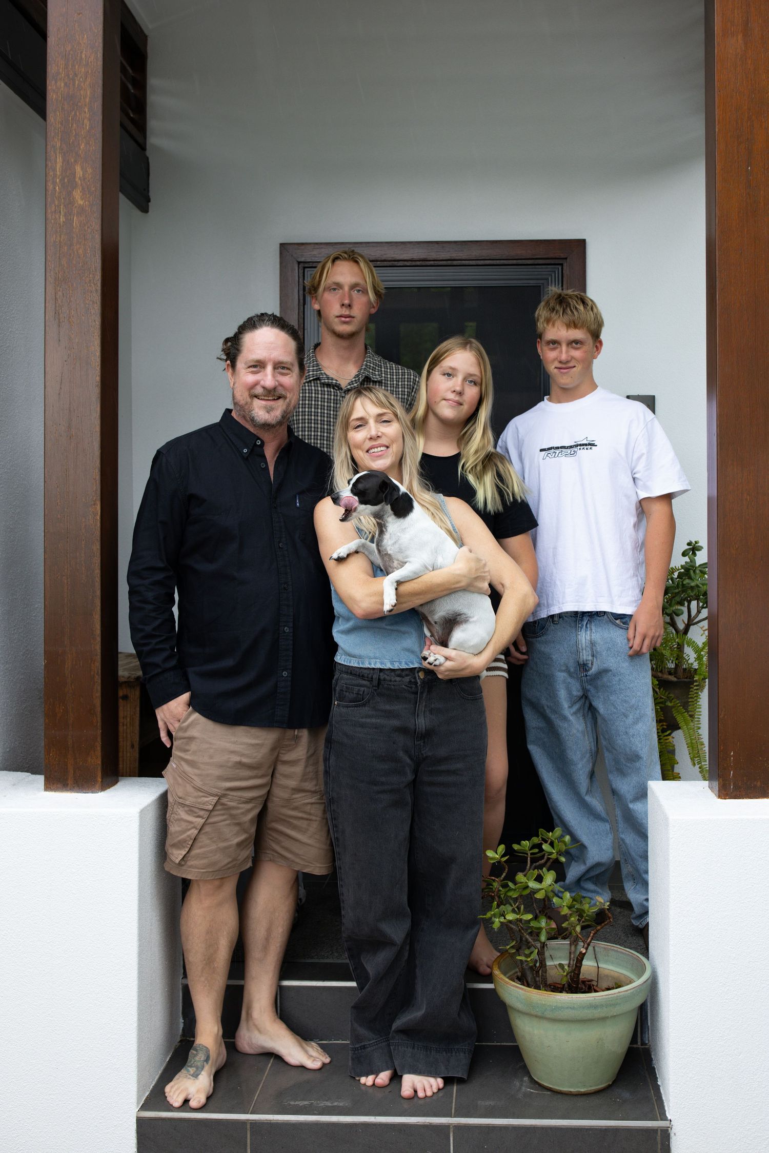 A group portrait of people and their cat standing together on a white porch.