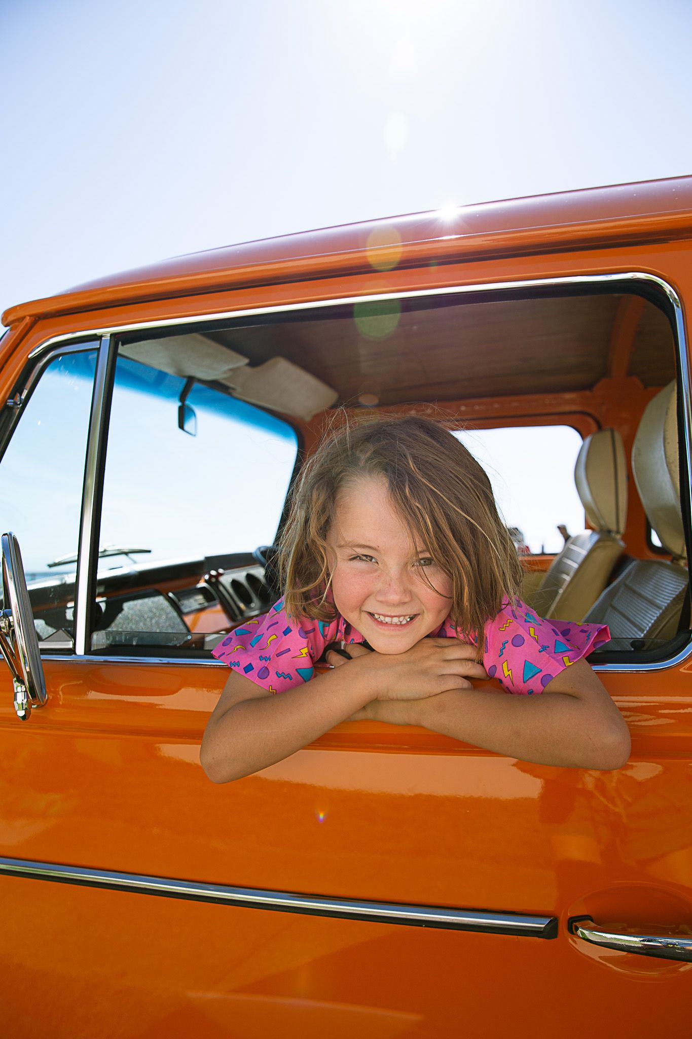 Orange vintage truck with decorative flowers in bright sunlight.