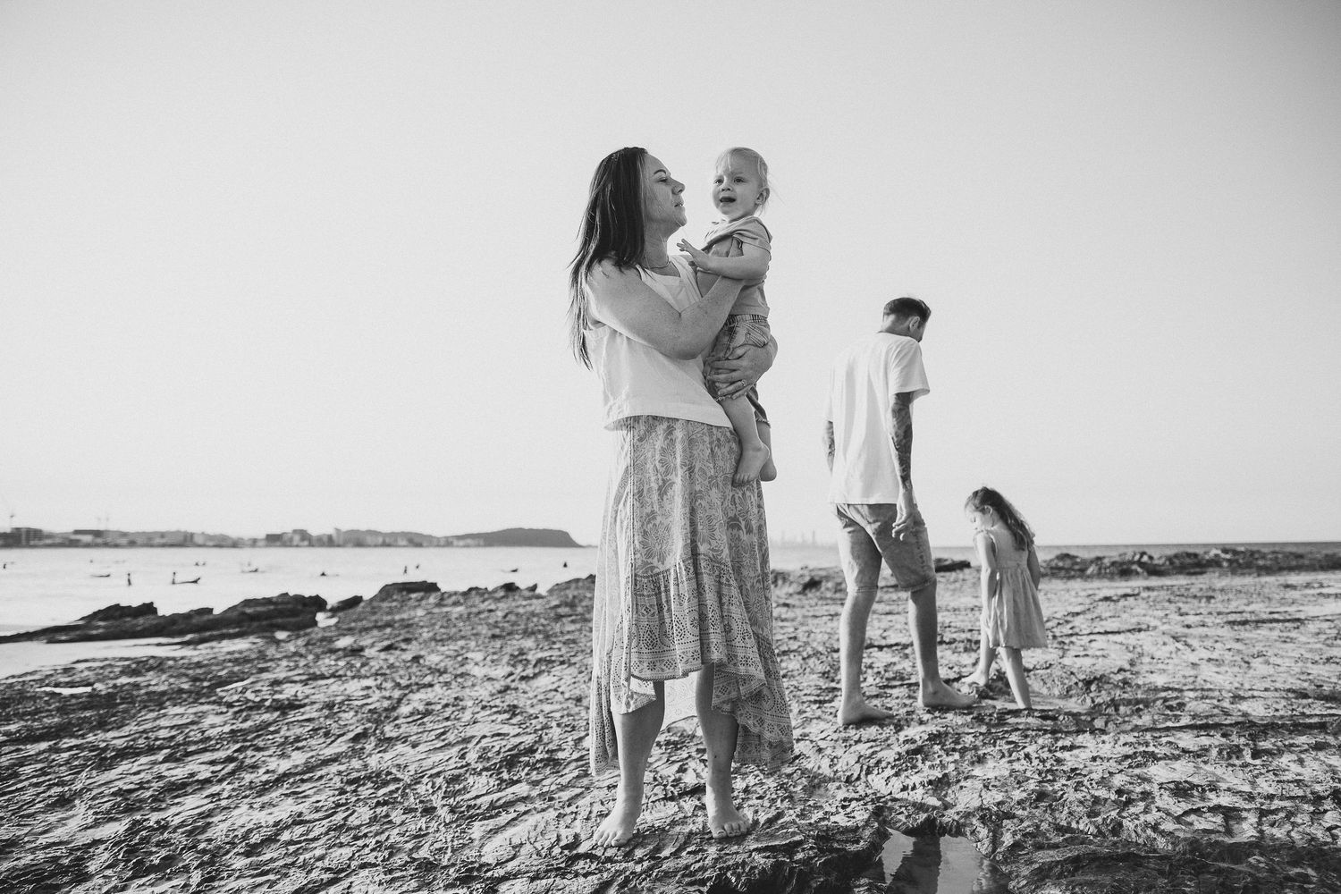 Family walking together along rocky coastline in black and white sequence.