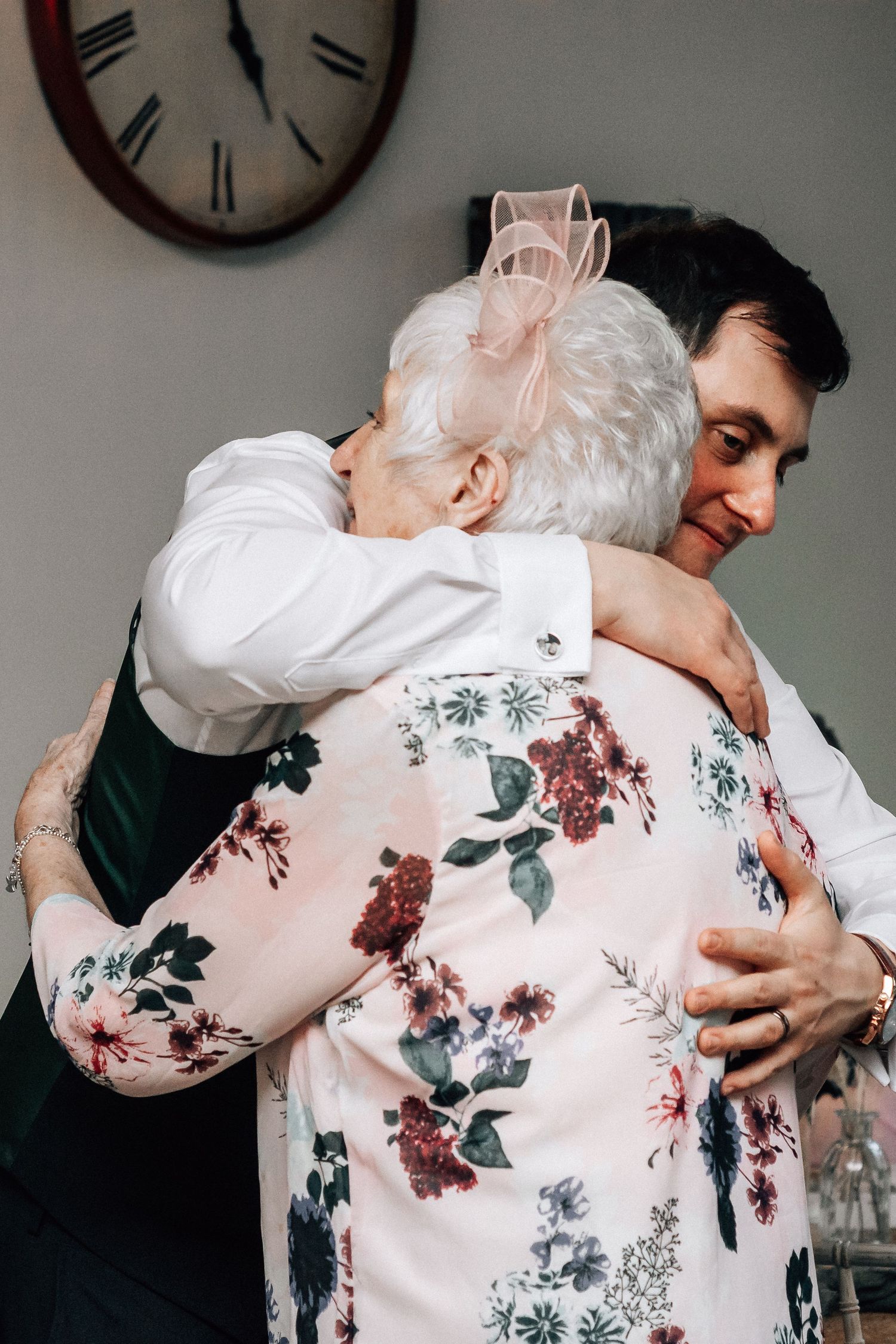 Elderly woman in floral dress sharing warm hug with younger guest at wedding celebration.