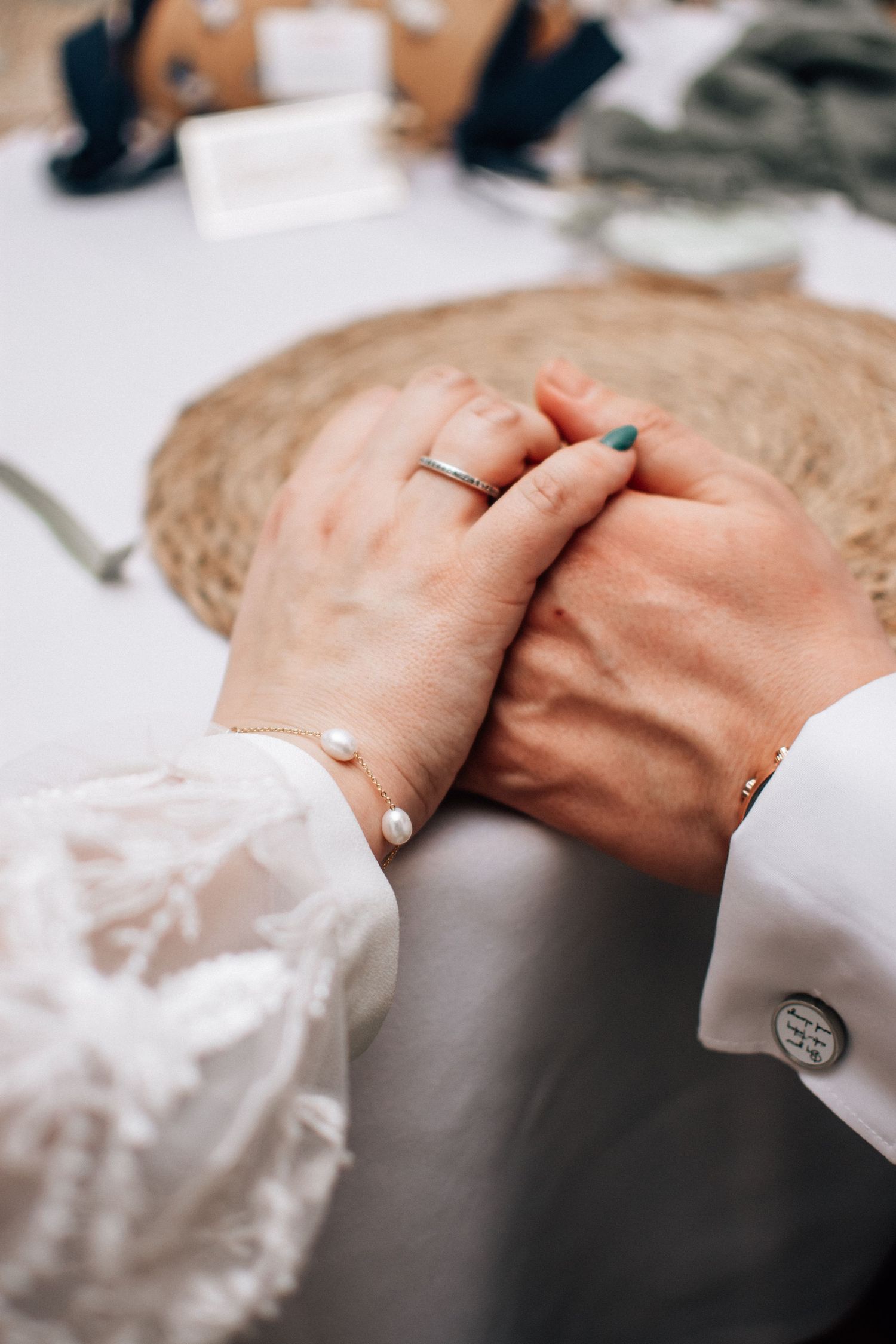 Close-up of couple holding hands at wedding table, woman wearing pearl bracelet and diamond ring.