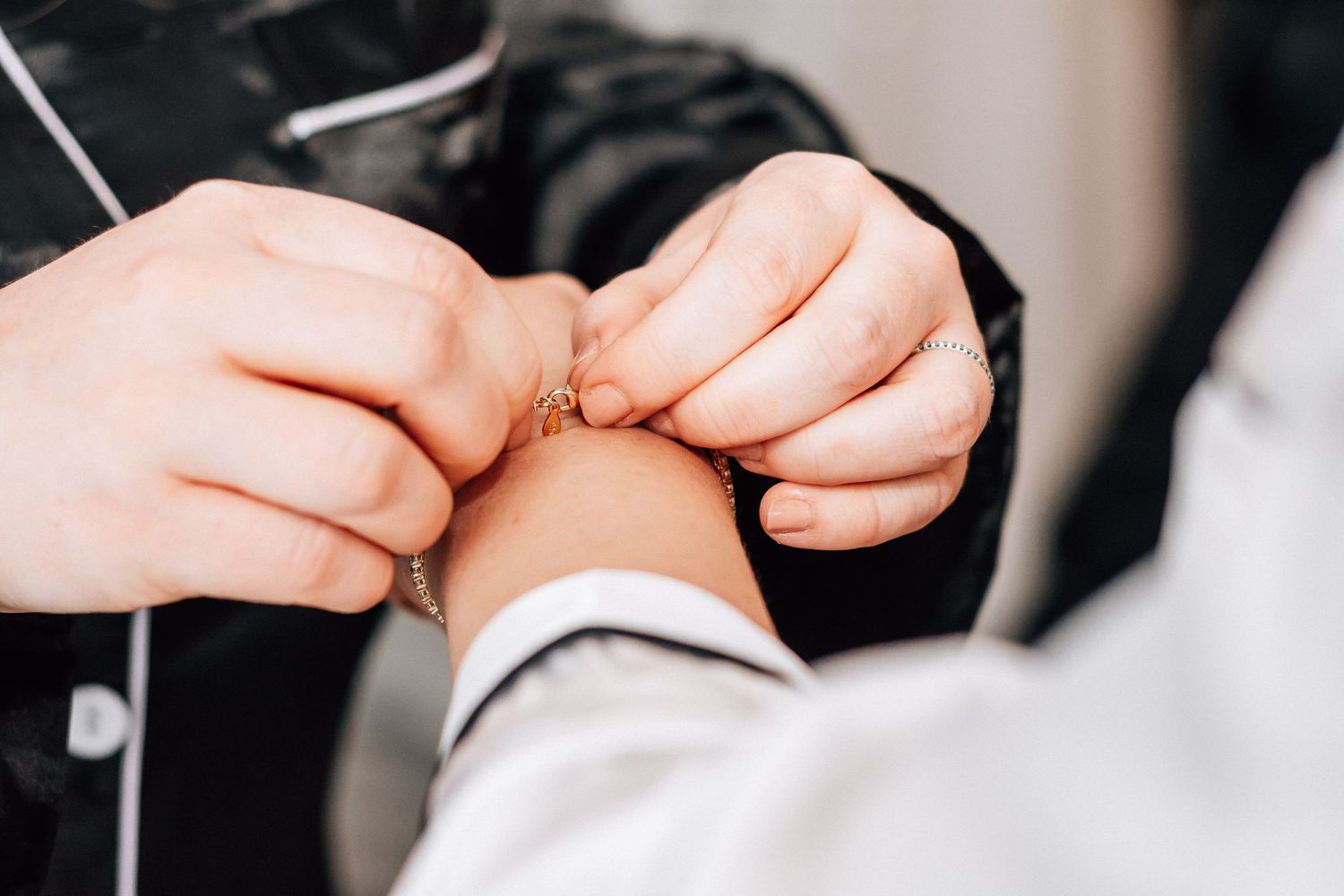Close-up of hands fastening a delicate gold bracelet on a wrist during a wedding preparation ceremony.