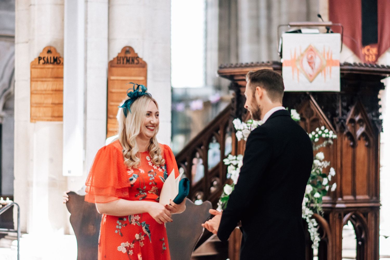 Couple exchanging vows in a church, bride wearing a red floral dress and groom in a black suit.
