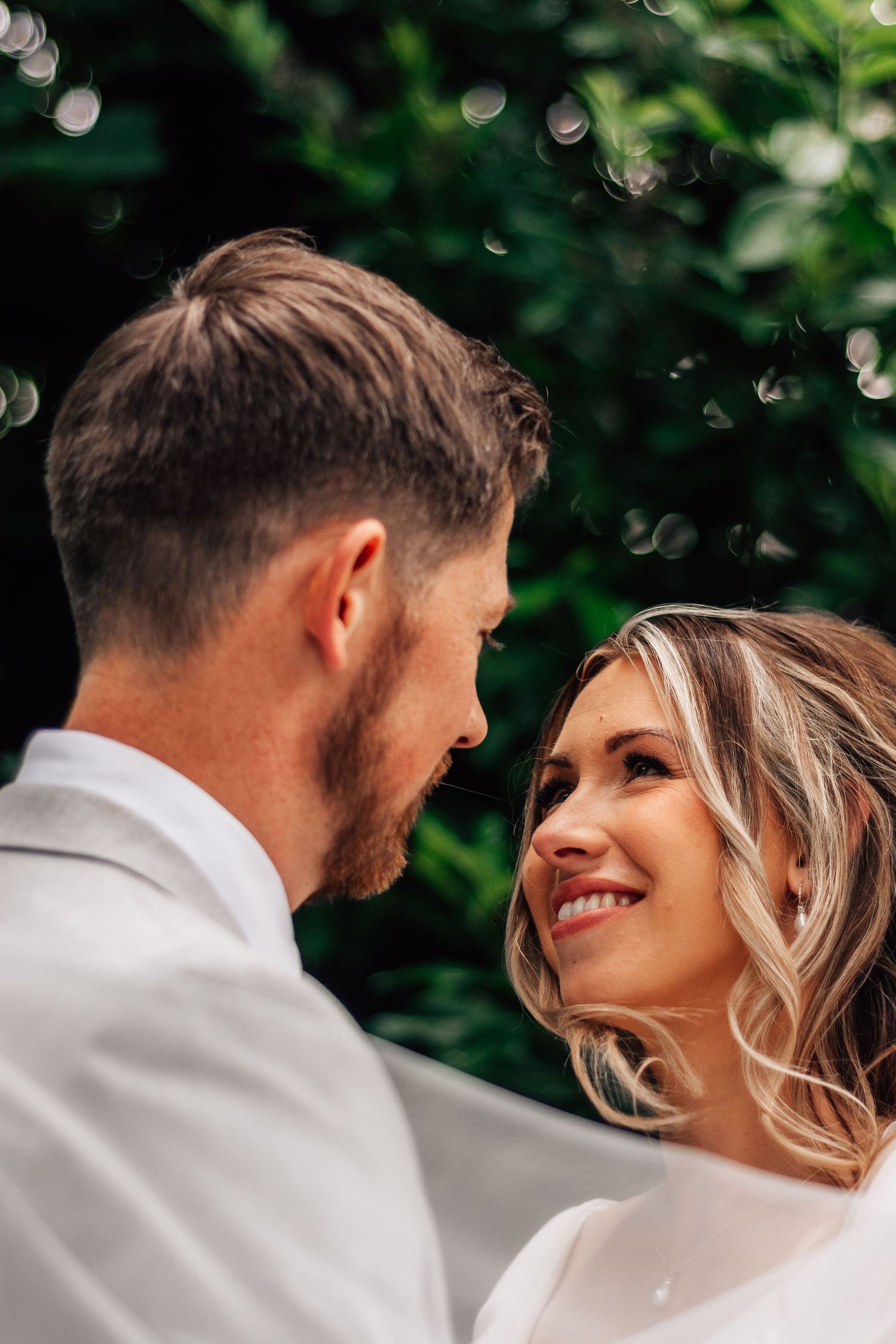 Smiling bride gazing up at groom with bokeh green background.