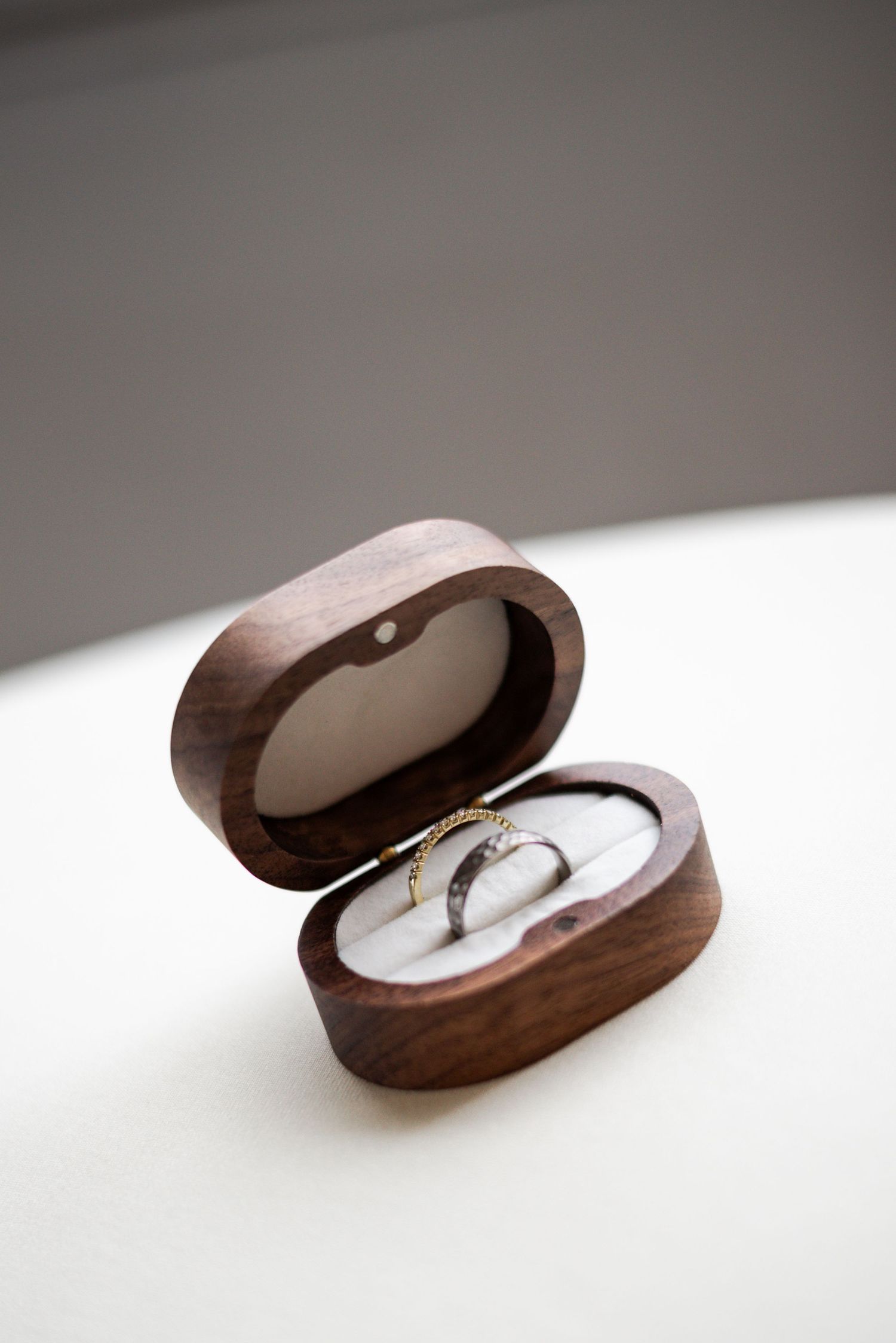 Elegant wedding rings displayed in an open oval wooden ring box with white velvet interior.