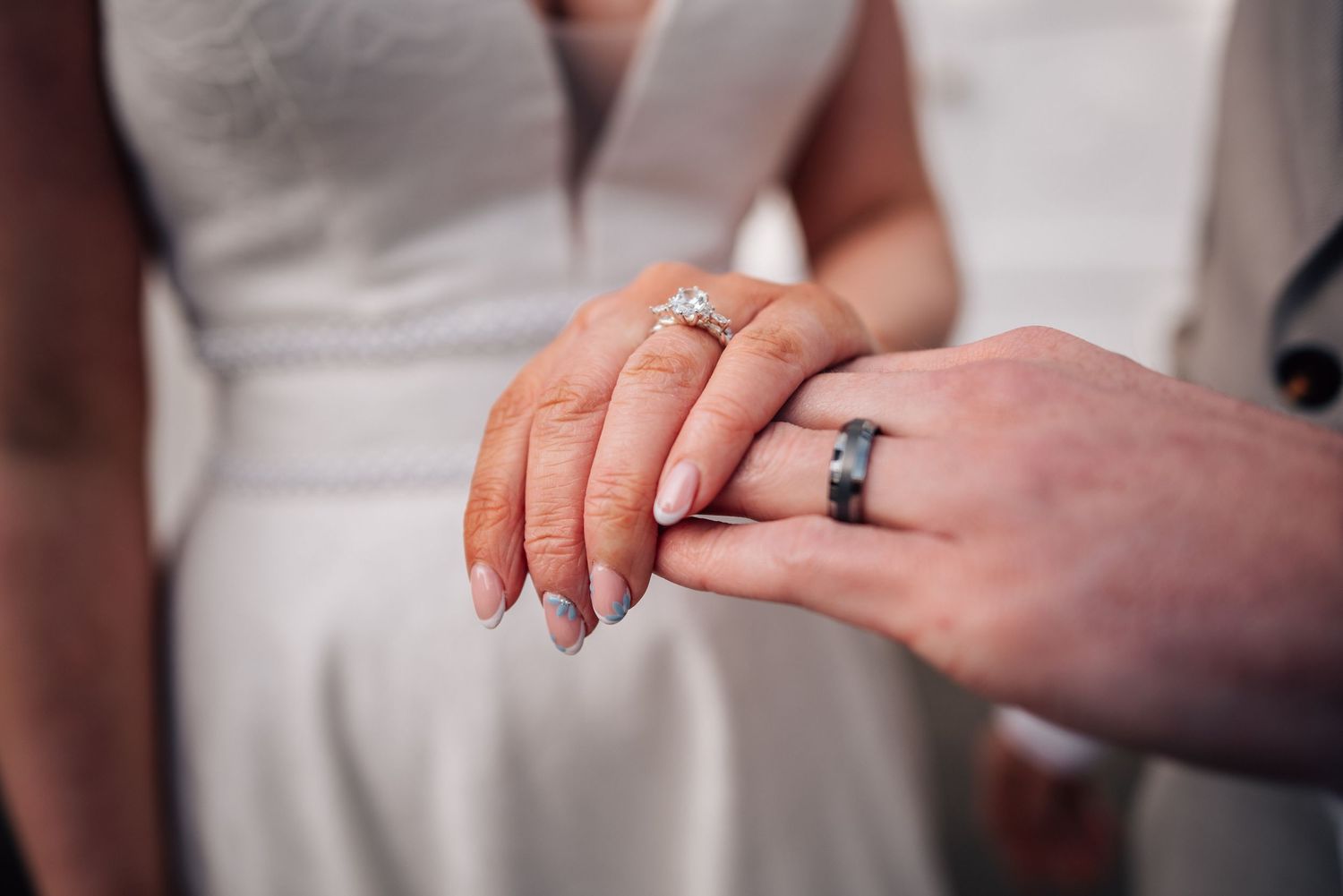 Close-up of newlyweds holding hands showing diamond engagement ring and wedding band during marriage ceremony.