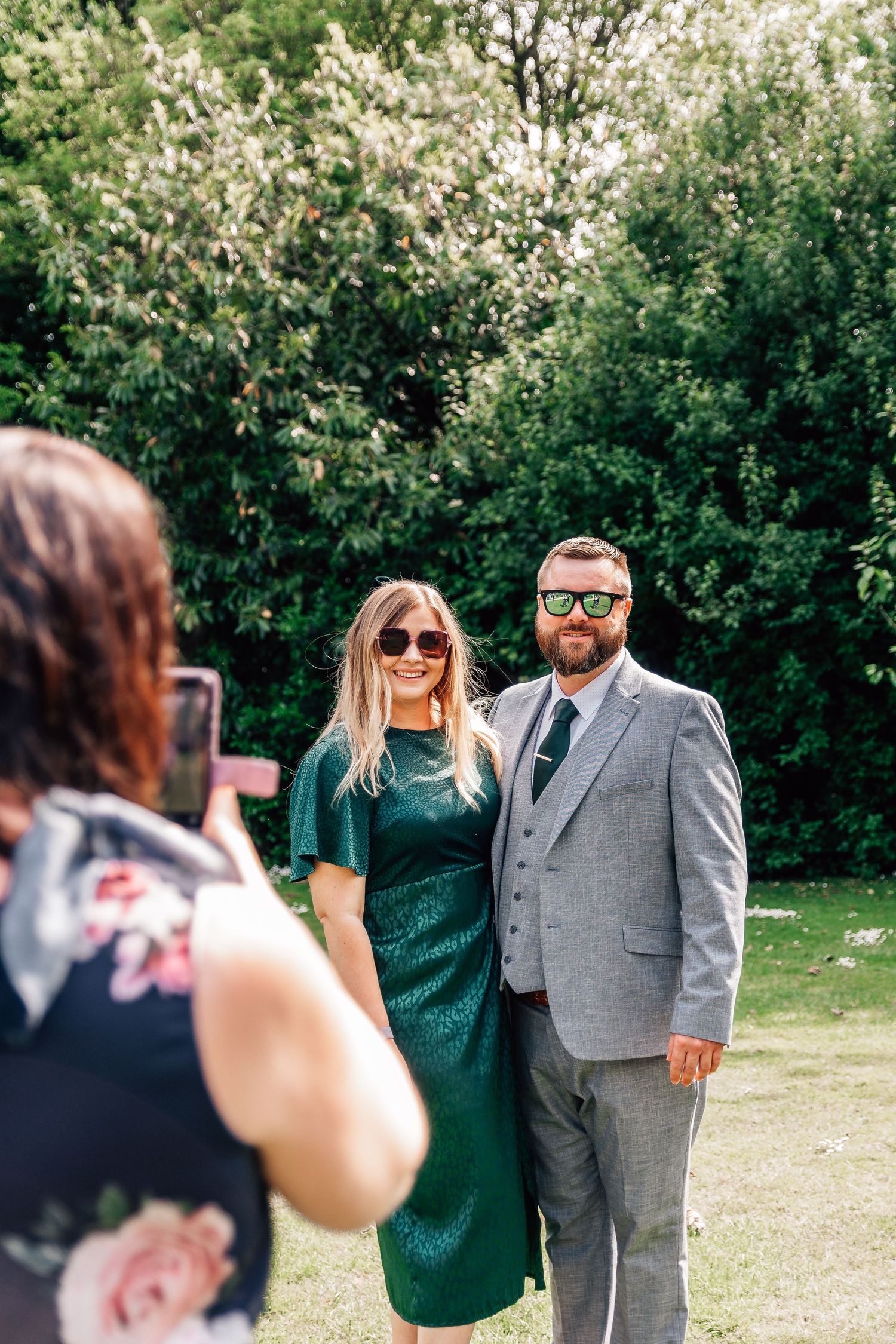 Wedding guests couple posing for photo in green sequin dress and grey suit.