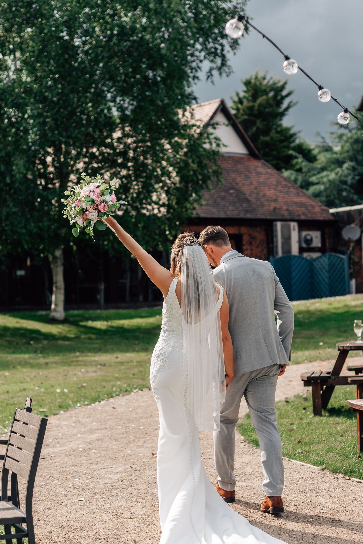 Bride raising bouquet while walking with groom through scenic wedding venue.