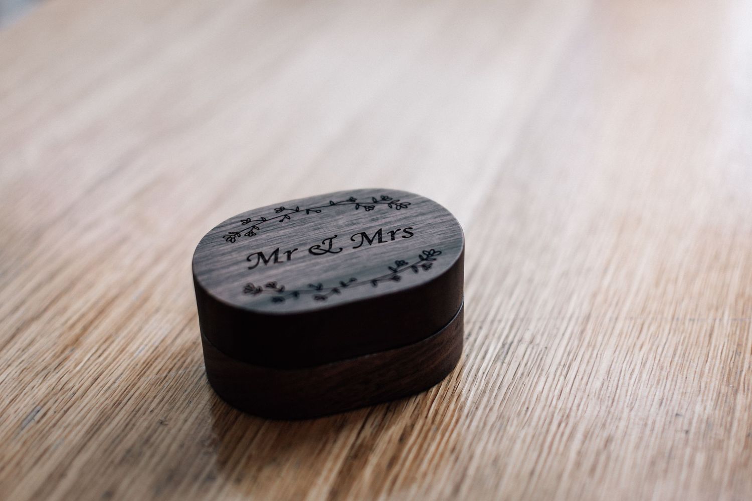 Dark wooden oval Mr & Mrs engraved wedding ring box on a light wood surface.