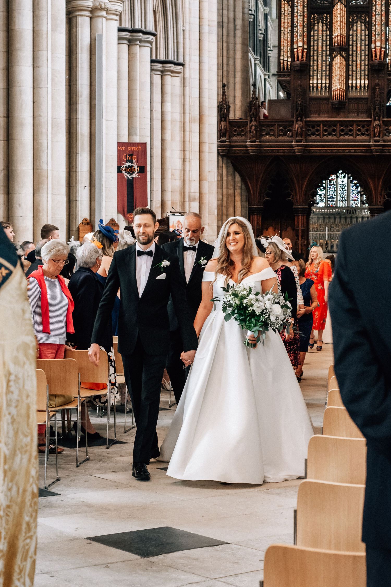 Newlyweds walk hand in hand down the aisle of a stunning cathedral after their wedding ceremony.