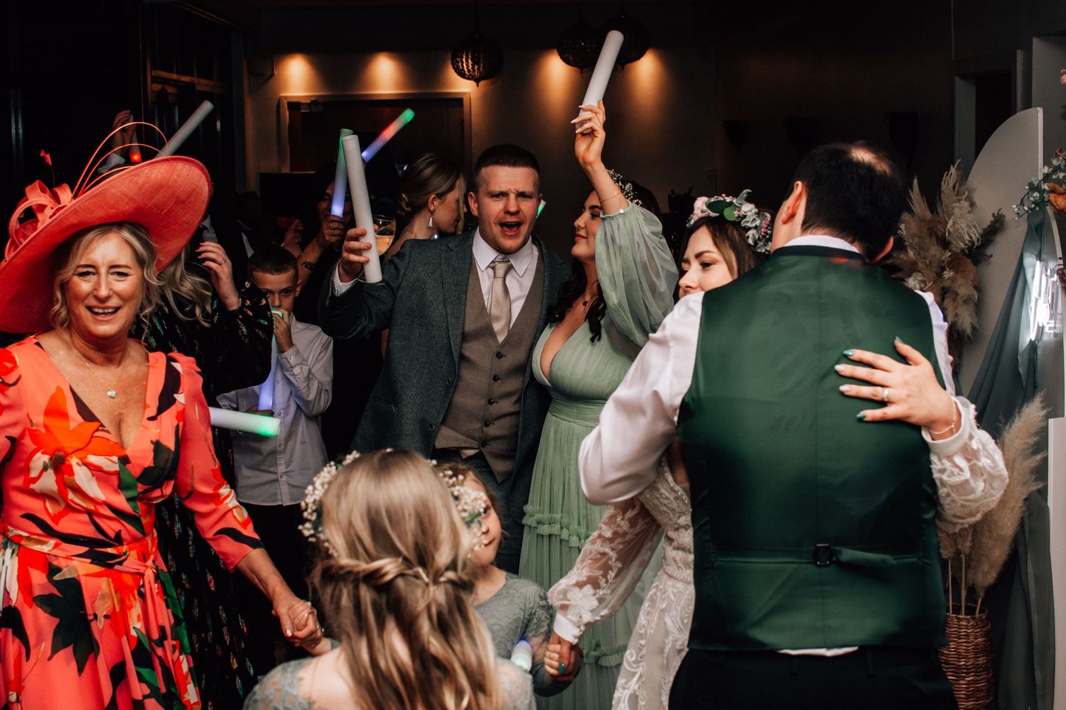 Excited wedding guests dancing and celebrating with glow sticks at lively wedding reception.