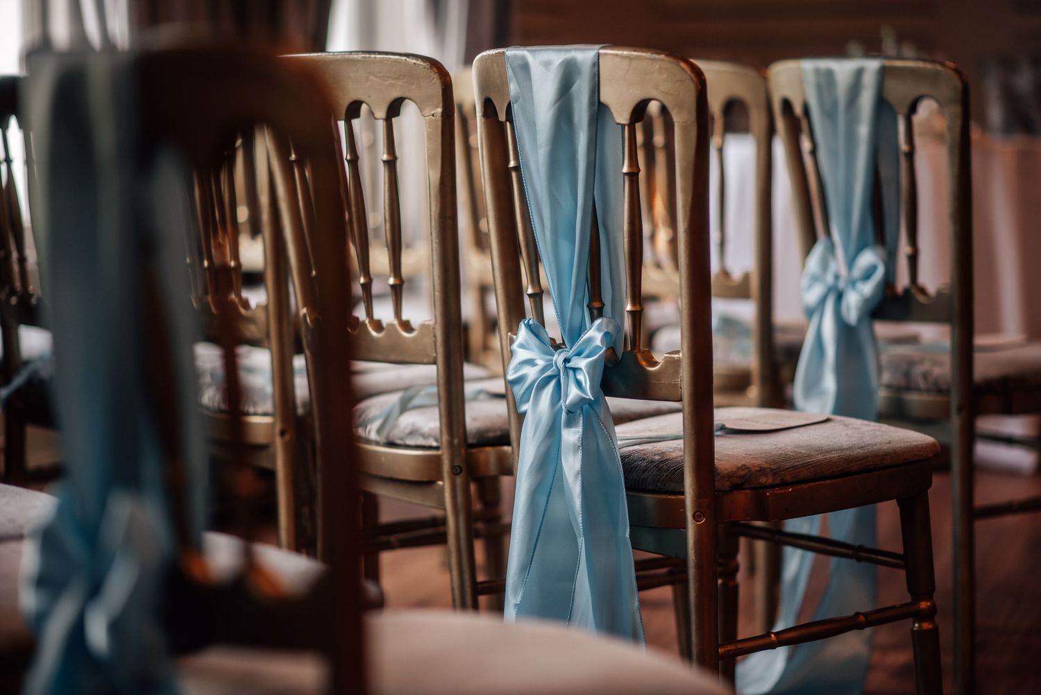 Wooden wedding chairs decorated with elegant light blue satin ribbon bows arranged in rows for a ceremony.