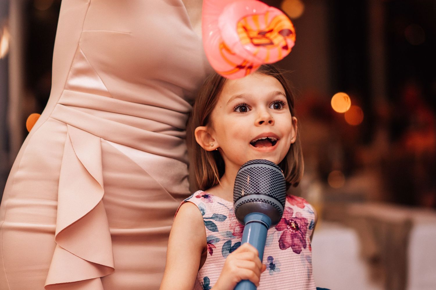 Young girl in floral dress singing into microphone at a party event.