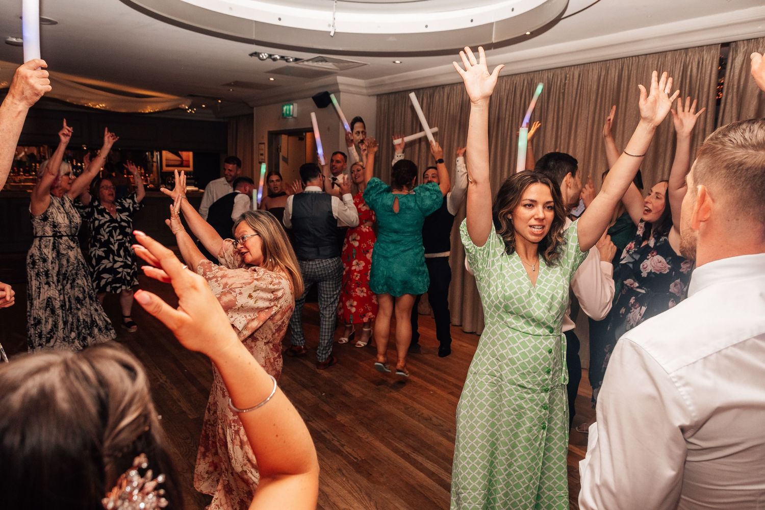 Excited guests dancing with hands raised at a lively wedding reception party.