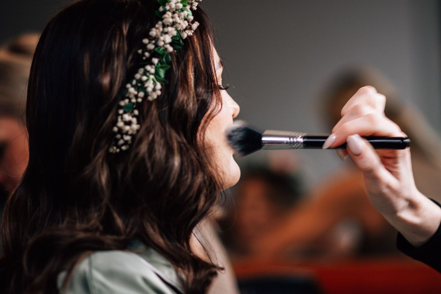 Makeup artist applying blush to a bride with floral crown in her dark hair before her wedding.
