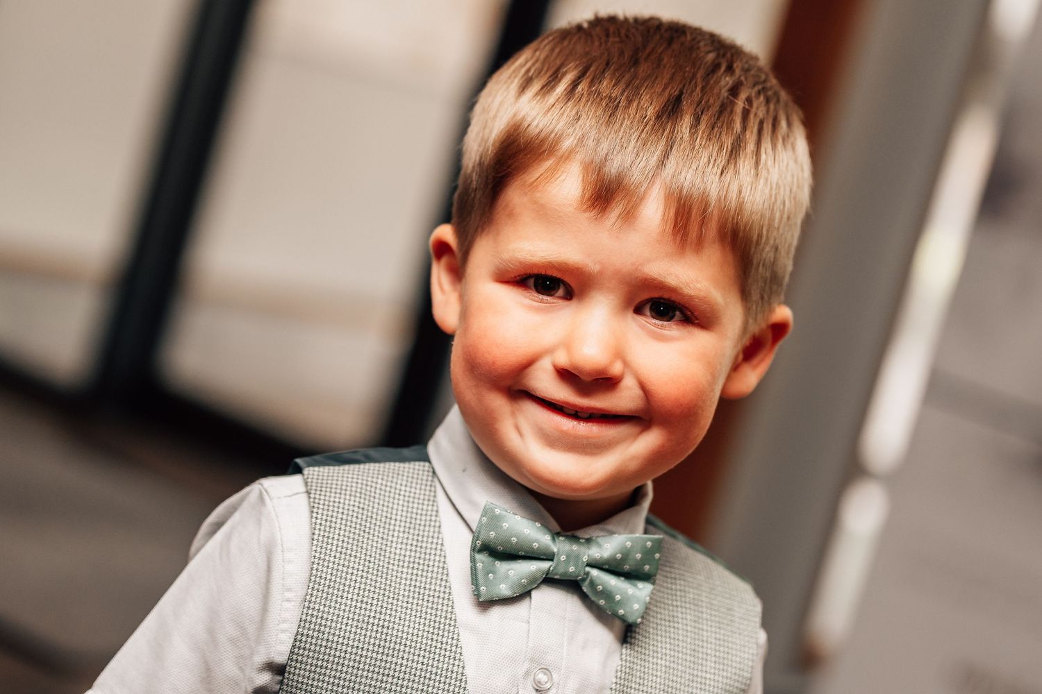 Smiling young boy wearing a gray vest and green bow tie, dressed up for a formal occasion.