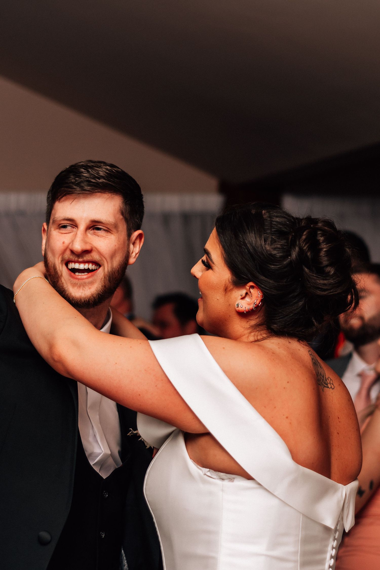 Laughing groom embraces his bride during their first dance at an intimate wedding reception.
