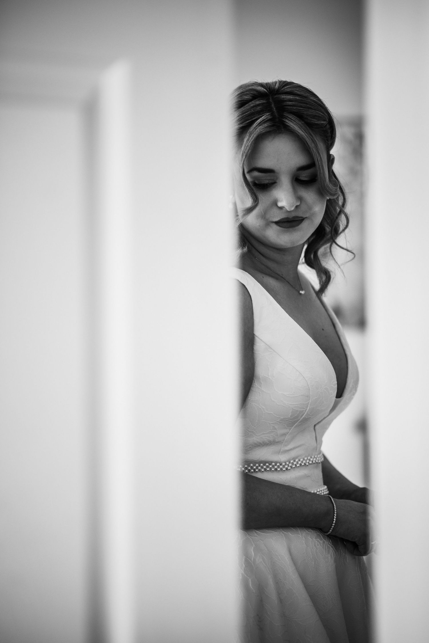 Black and white photo of a bride in a deep V-neck wedding dress with a beaded belt, looking down elegantly.