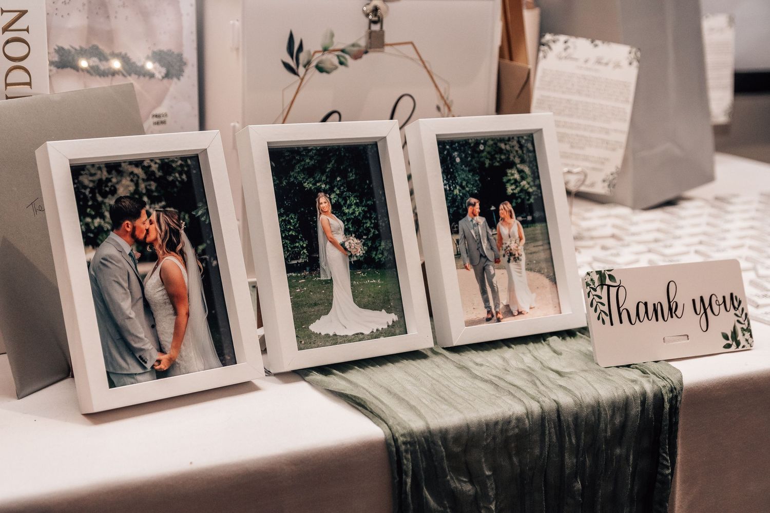 Three framed wedding photos displayed on a table with a green velvet runner and a thank you card at a reception.