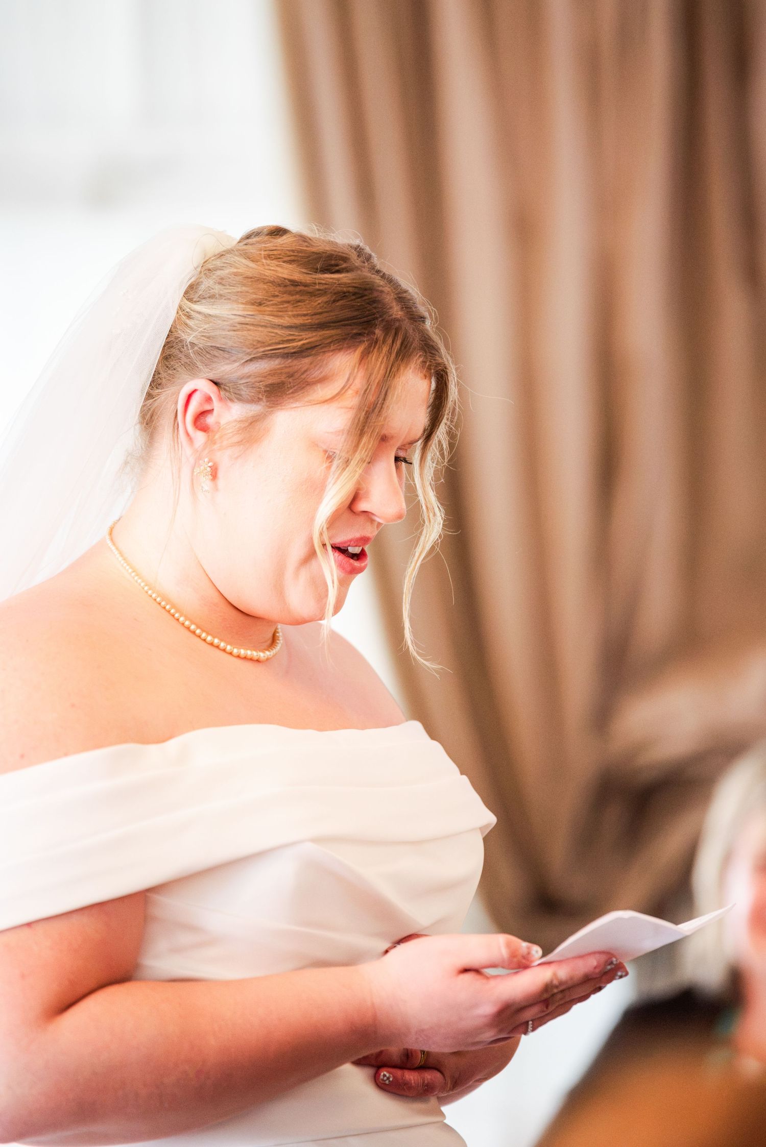 Emotional bride in white gown and veil reading a heartfelt letter on her wedding day.