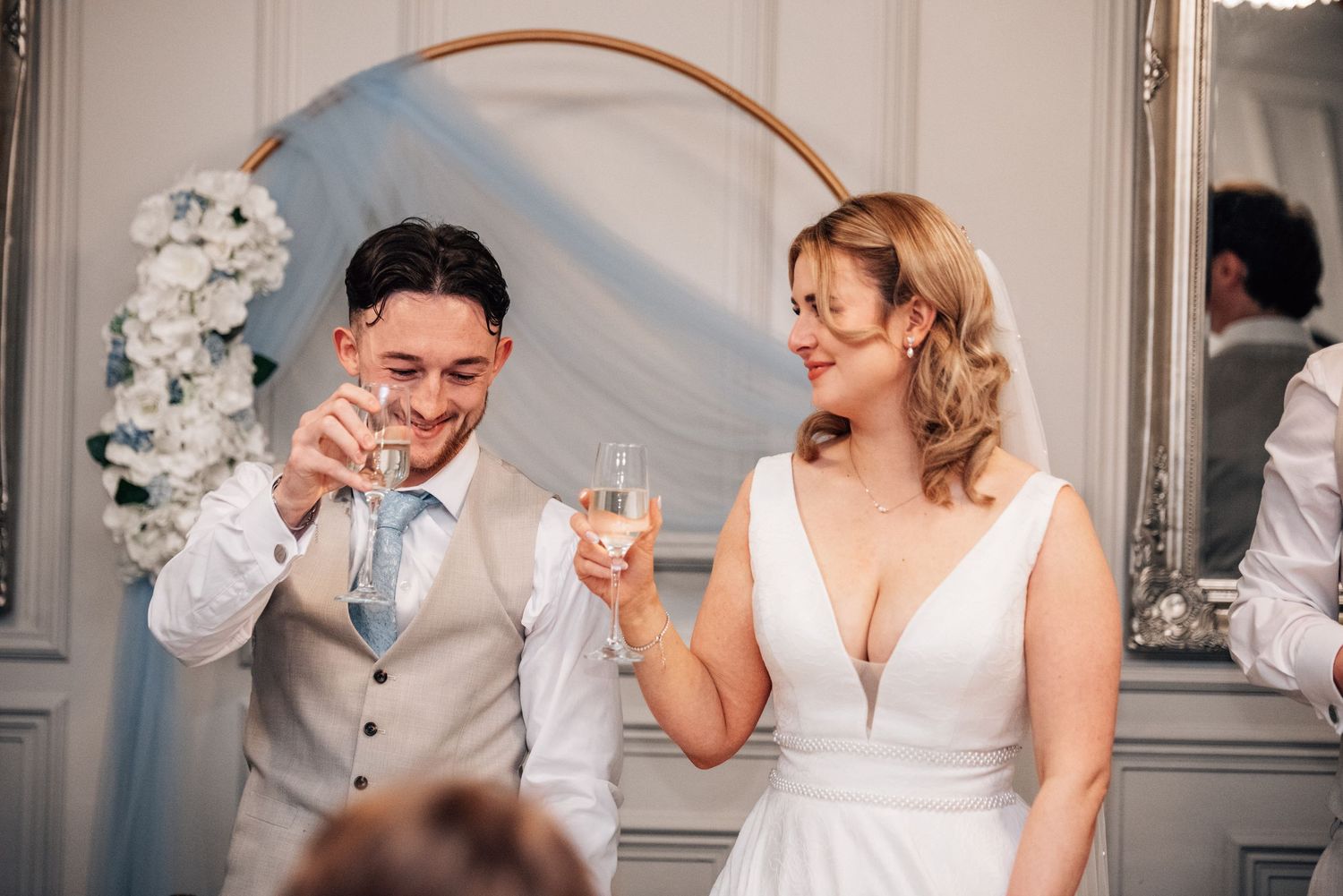 Bride and groom smiling and toasting with champagne glasses at their wedding reception indoors.