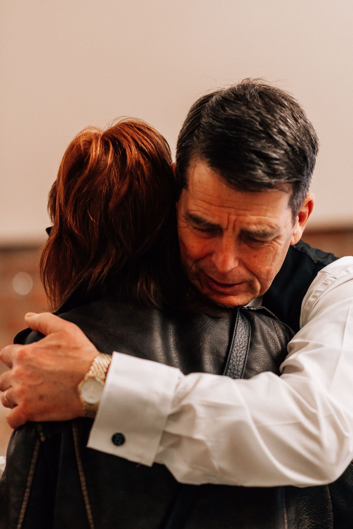 Two people share a heartfelt embrace, with a man in a white shirt and vest hugging a redheaded woman.
