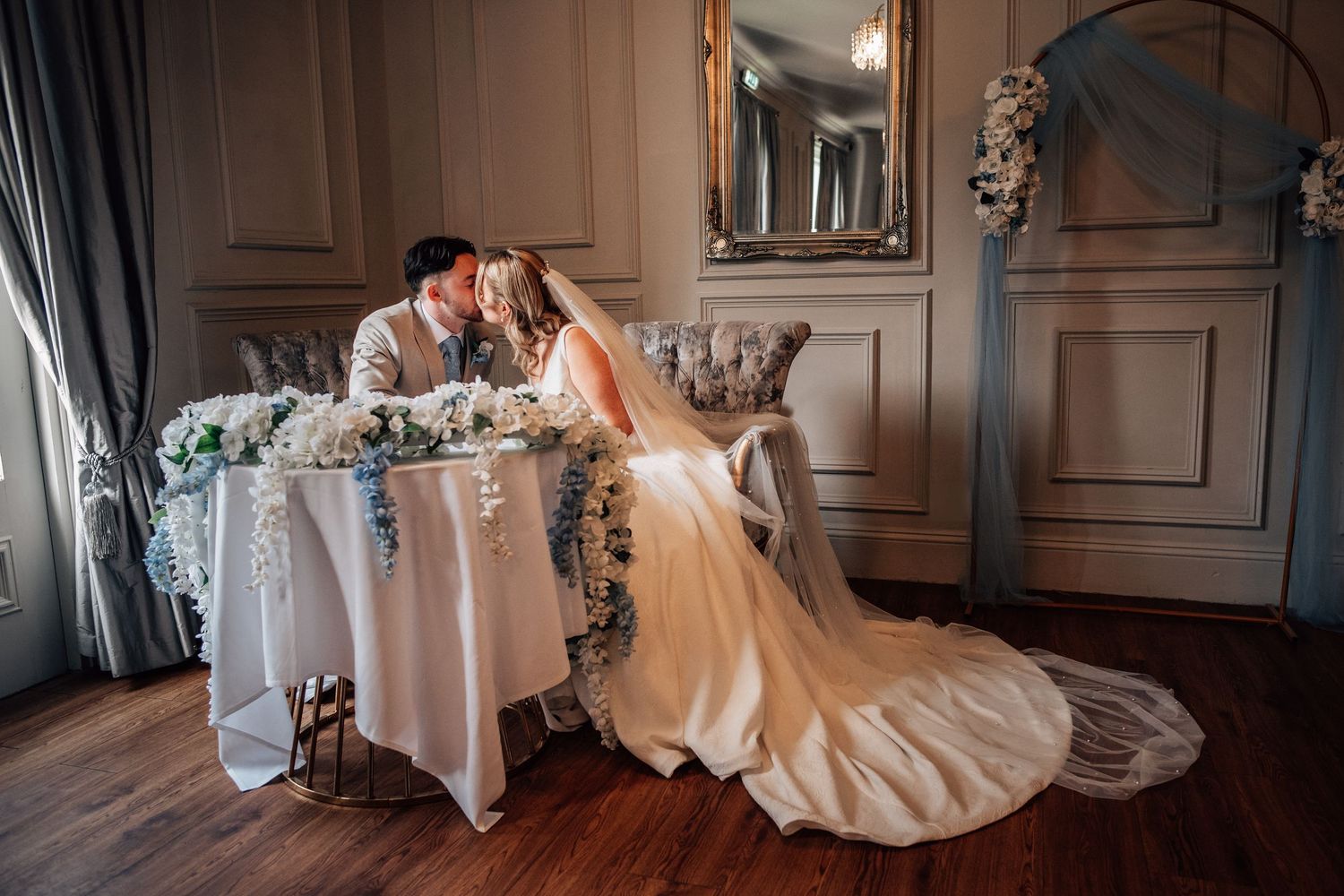 Bride and groom sharing a romantic kiss at their floral-decorated wedding sweetheart table.