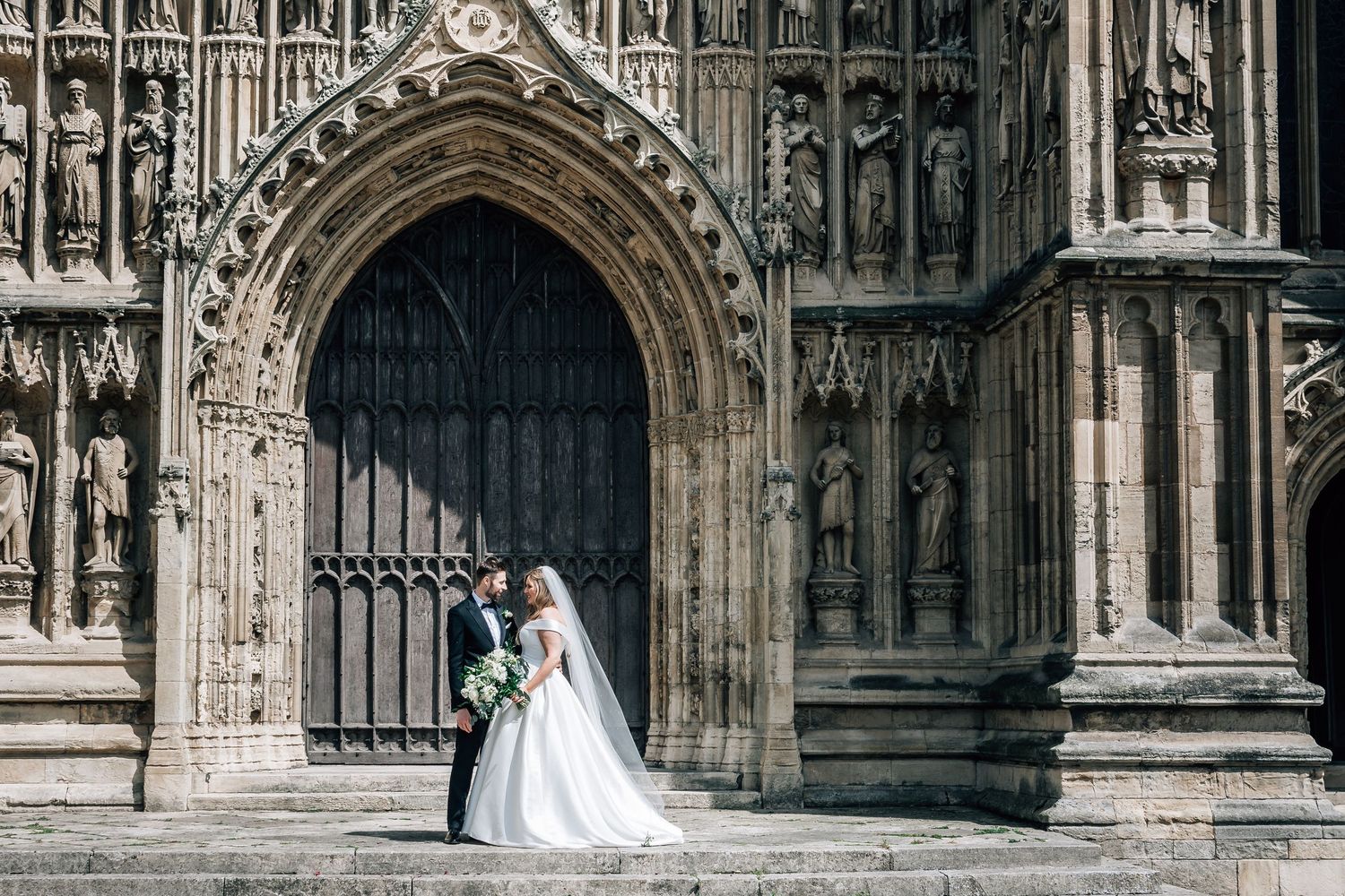 Bride and groom share a romantic moment outside an ornate Gothic cathedral entrance on their wedding day.