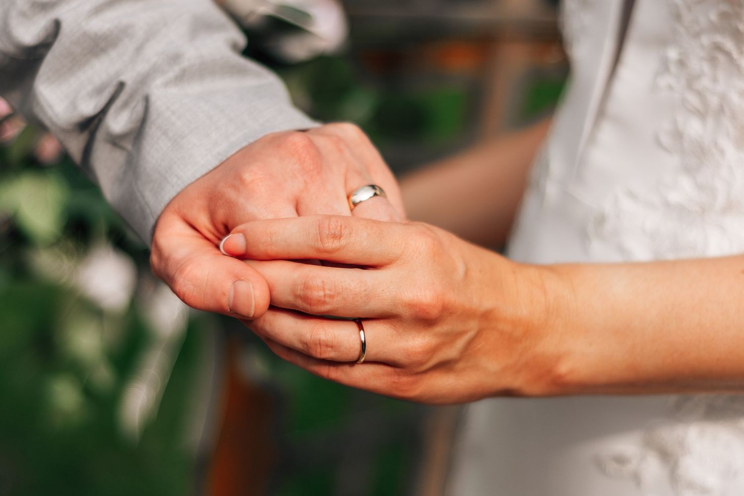 Close-up of newlyweds exchanging wedding rings during marriage ceremony, showing gold bands on fingers.