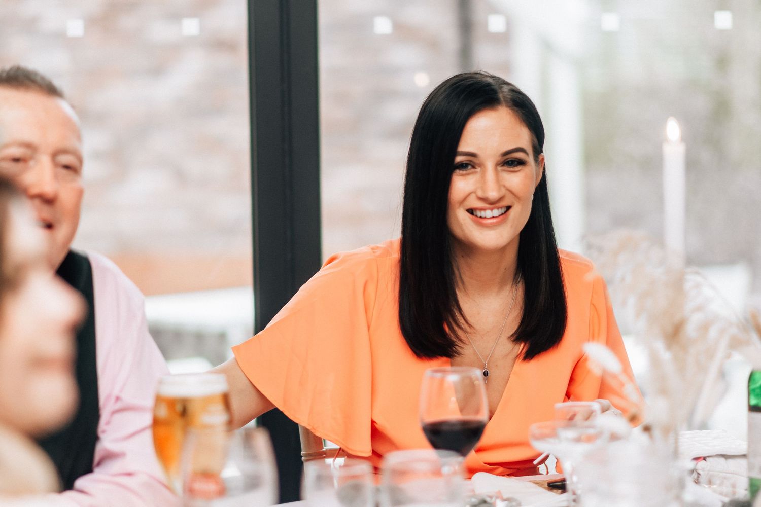 Elegant woman in orange dress smiling at a wedding reception dinner table.