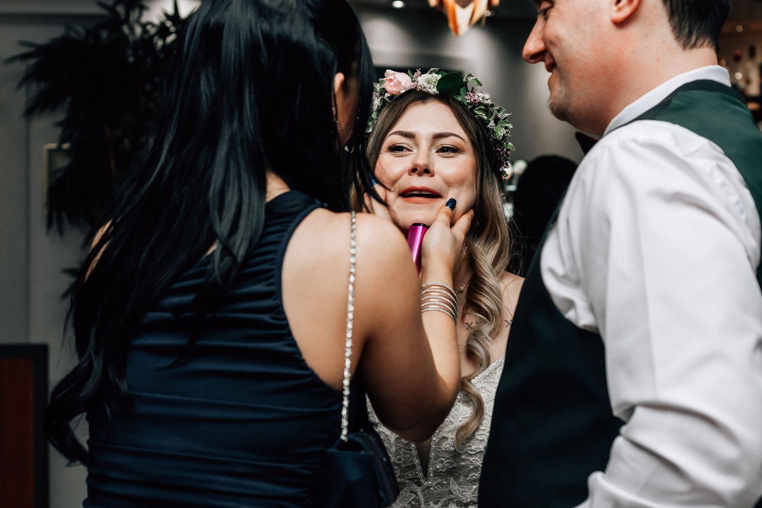 Bride with flower crown laughing joyfully with guests at wedding reception party.