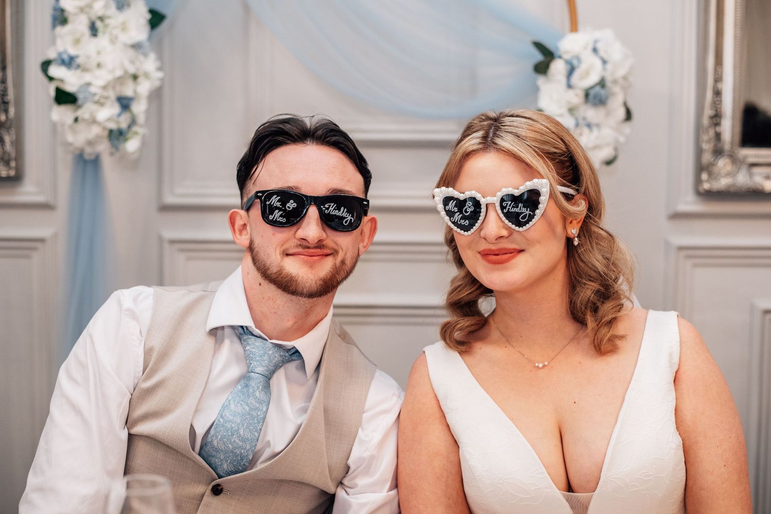 Bride and groom wearing fun sunglasses at wedding reception with blue floral decorations.