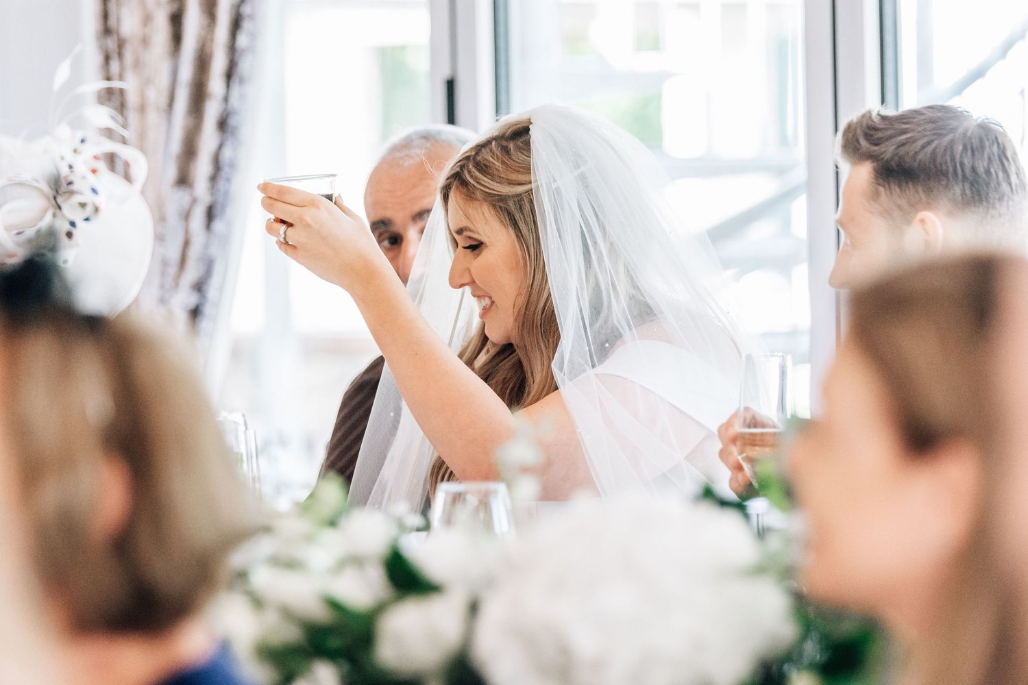 Bride laughing with guest at wedding reception table adorned with white floral arrangements.