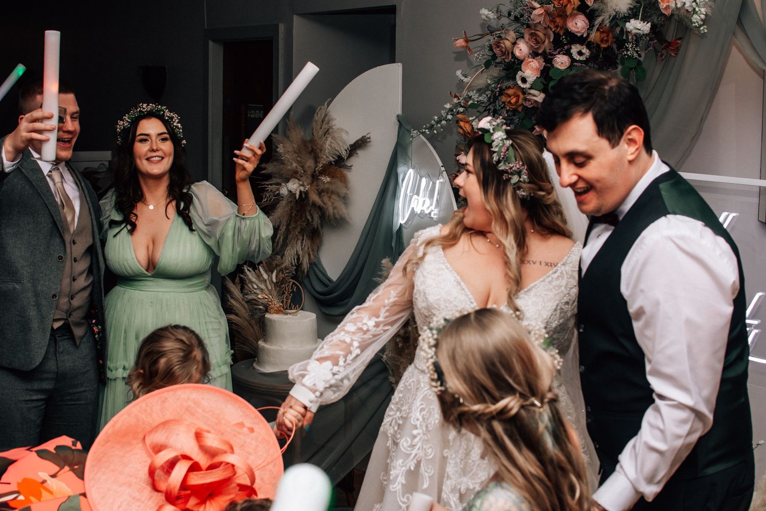 Bride and groom holding hands during wedding ceremony surrounded by guests with floral arch backdrop.