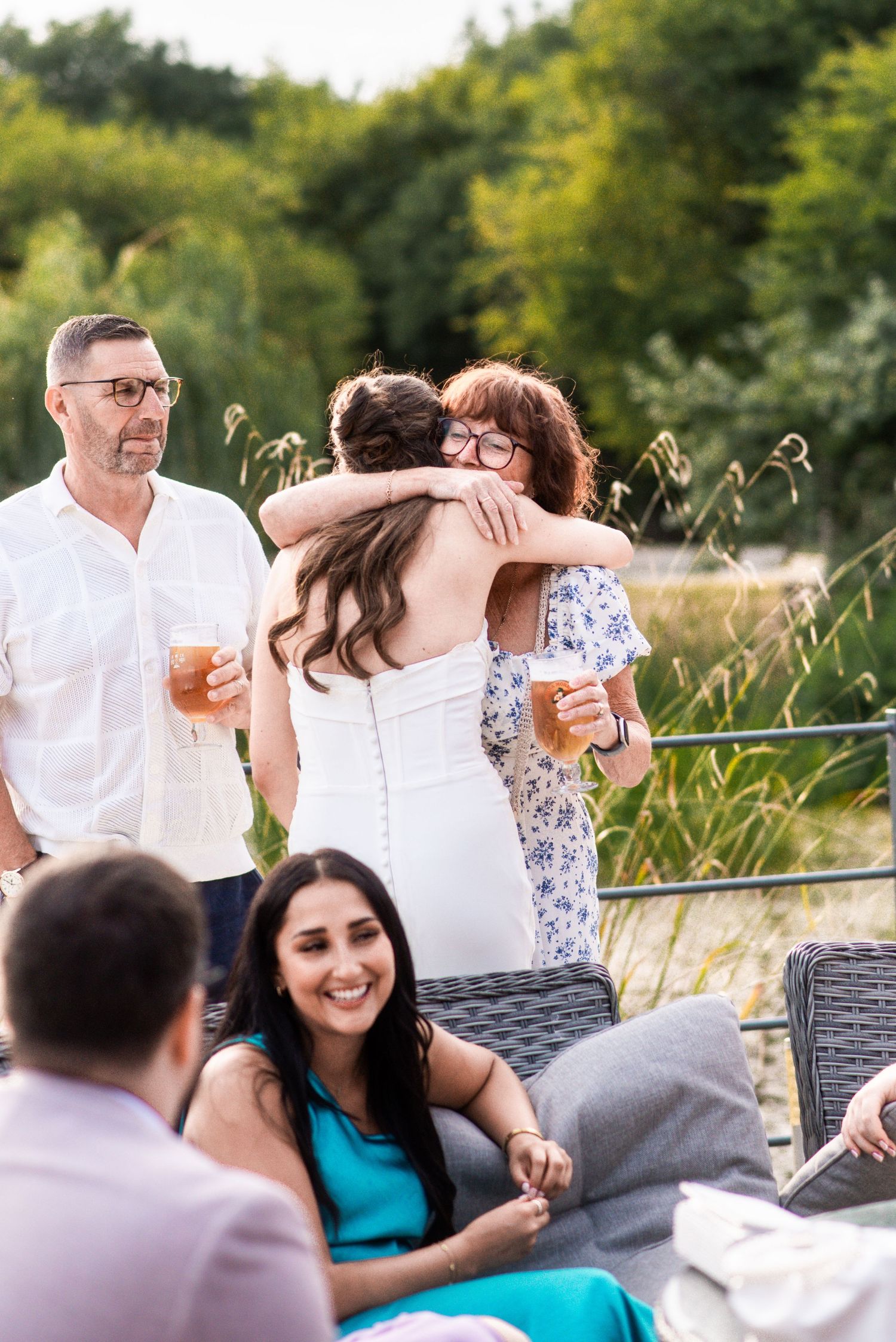 Friends and family hugging and socializing outdoors at a summer garden party with drinks.