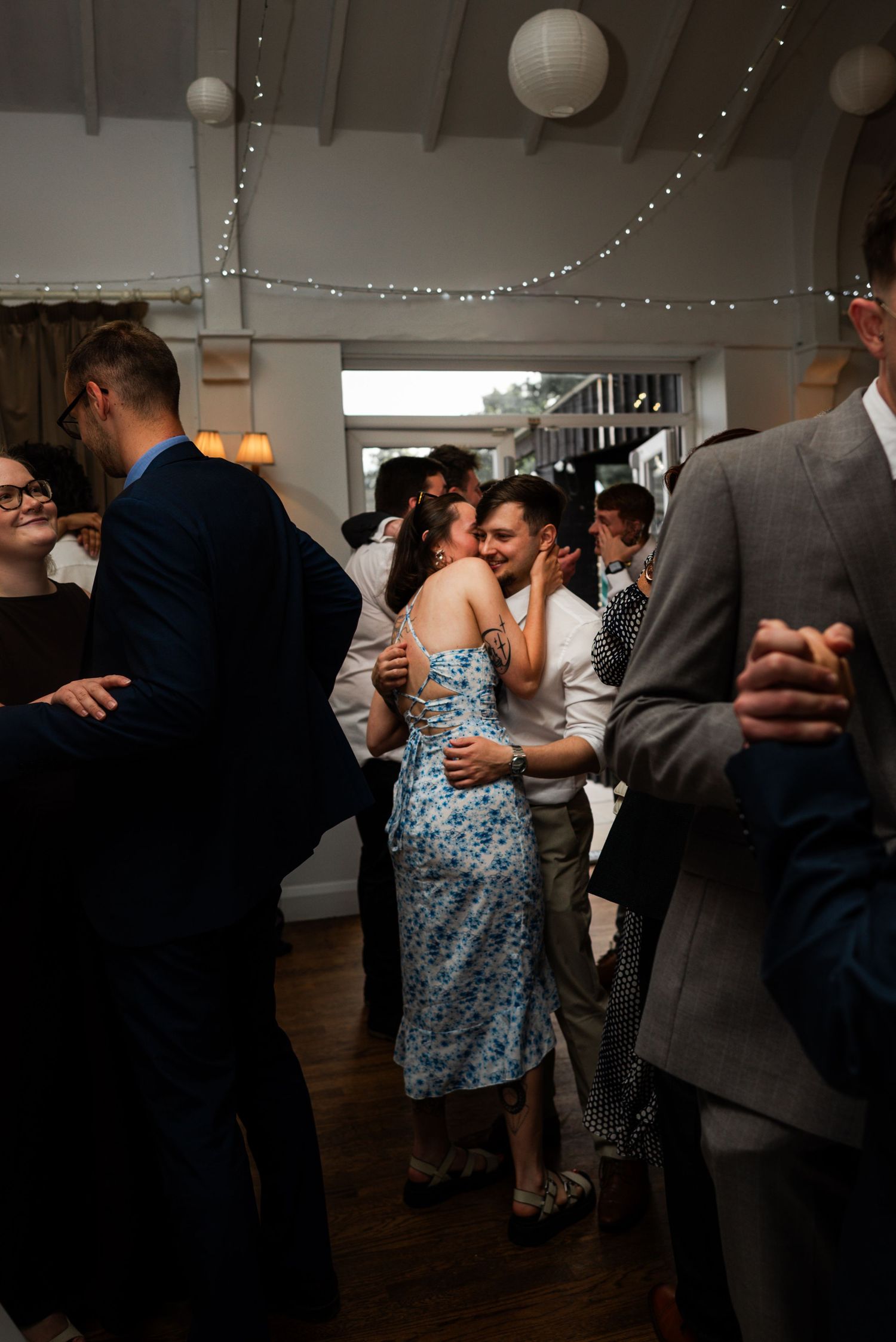 Couple kissing on the dance floor surrounded by guests at a wedding reception.