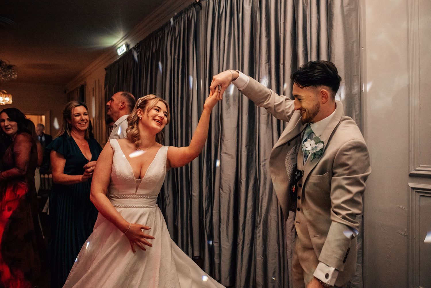 Bride in white gown dancing with groom in grey suit during lively wedding reception celebration.
