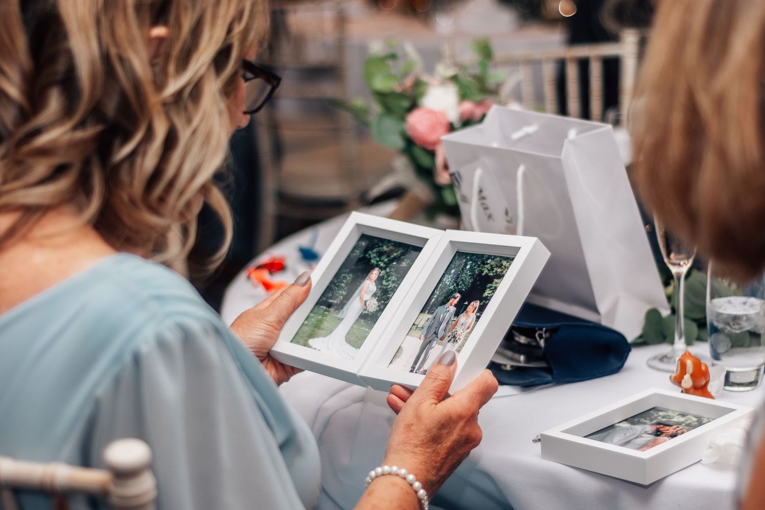 Woman in blue dress viewing a wedding photo album at a reception table with flowers and champagne glasses.